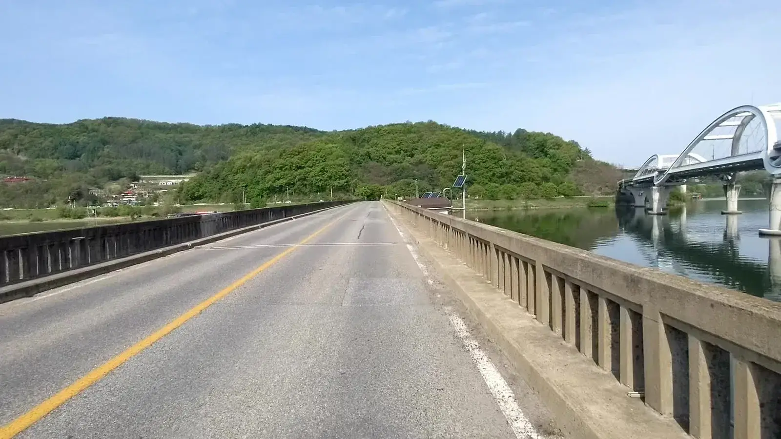A broad bridge crossing a river between green hills