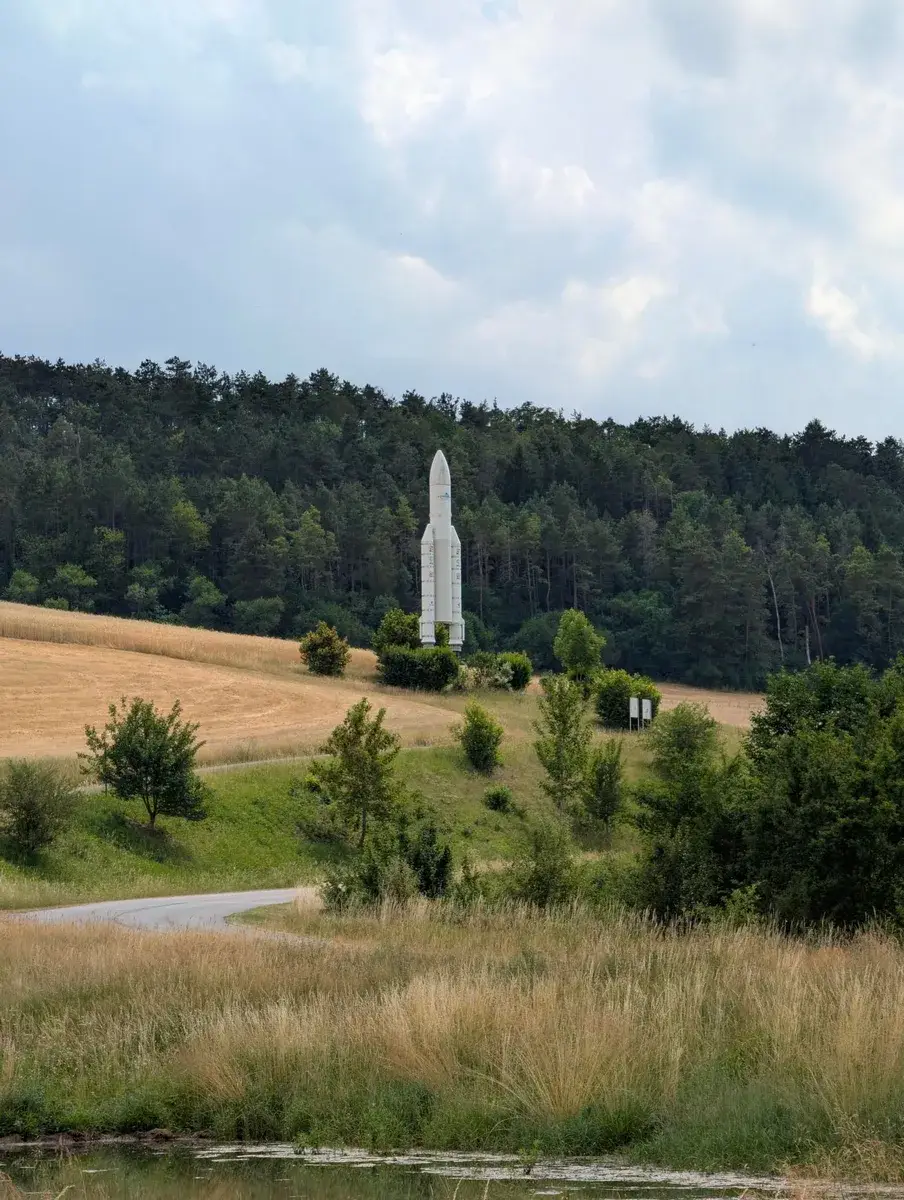 A tall pale monument standing above a forest clearing