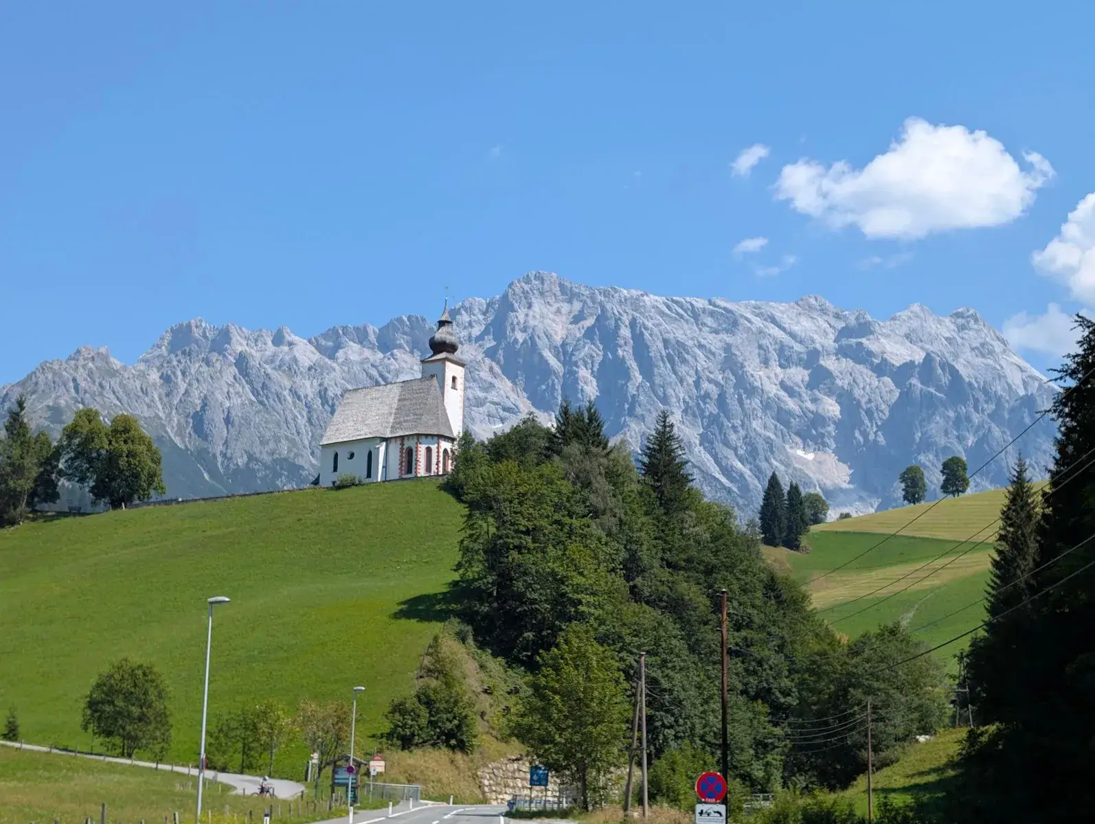 A white hillside chapel beneath a craggy alpine ridge