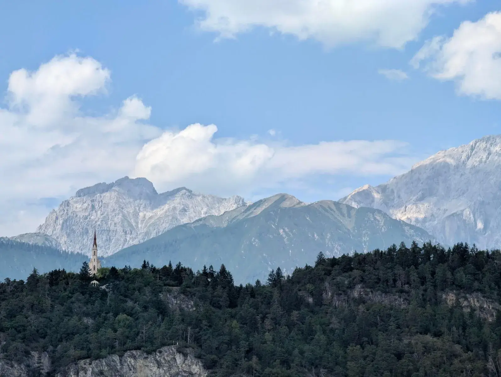 Layered limestone mountains beneath bright summer cloud