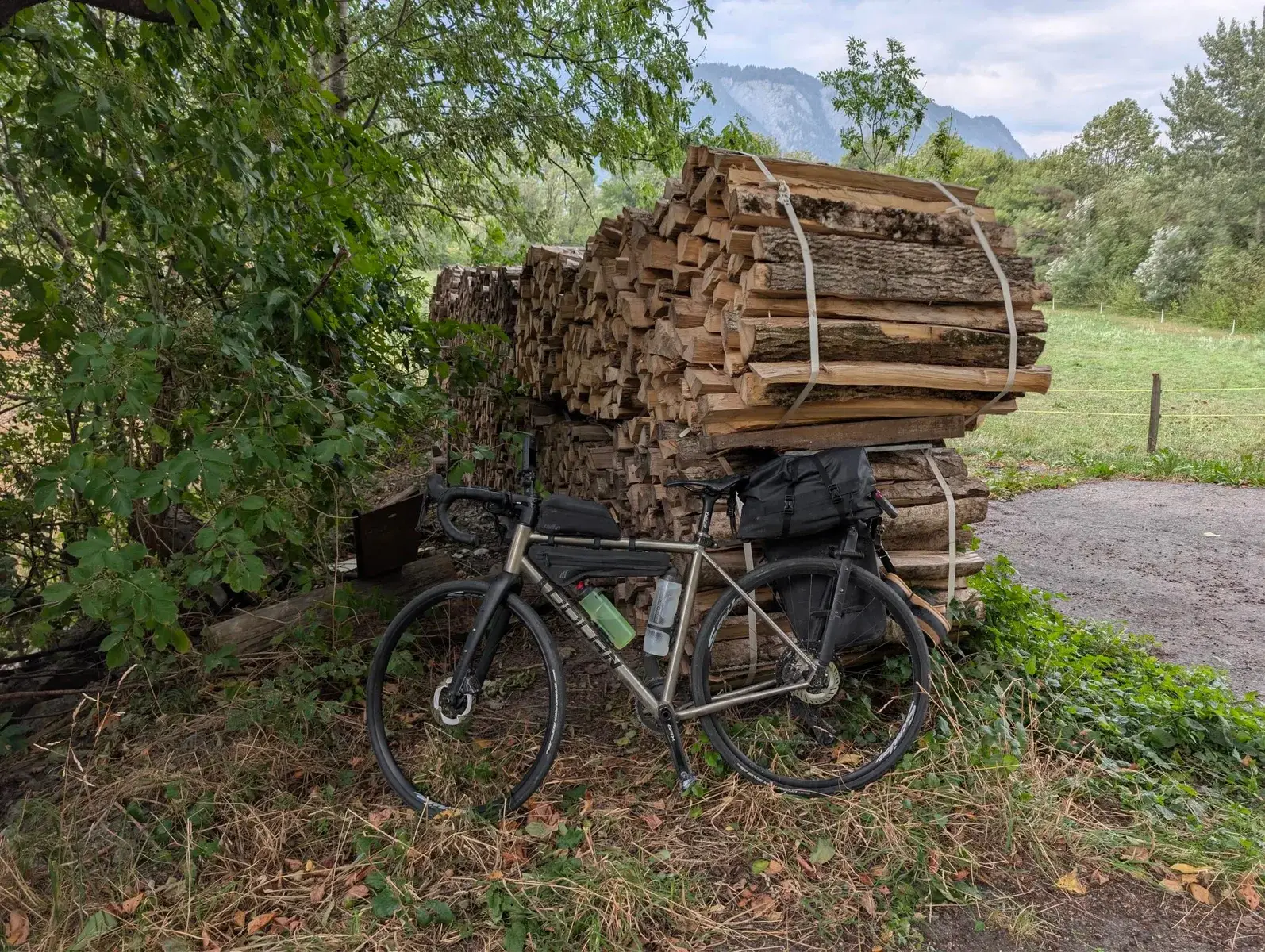 A touring bicycle resting beside a tall stack of firewood