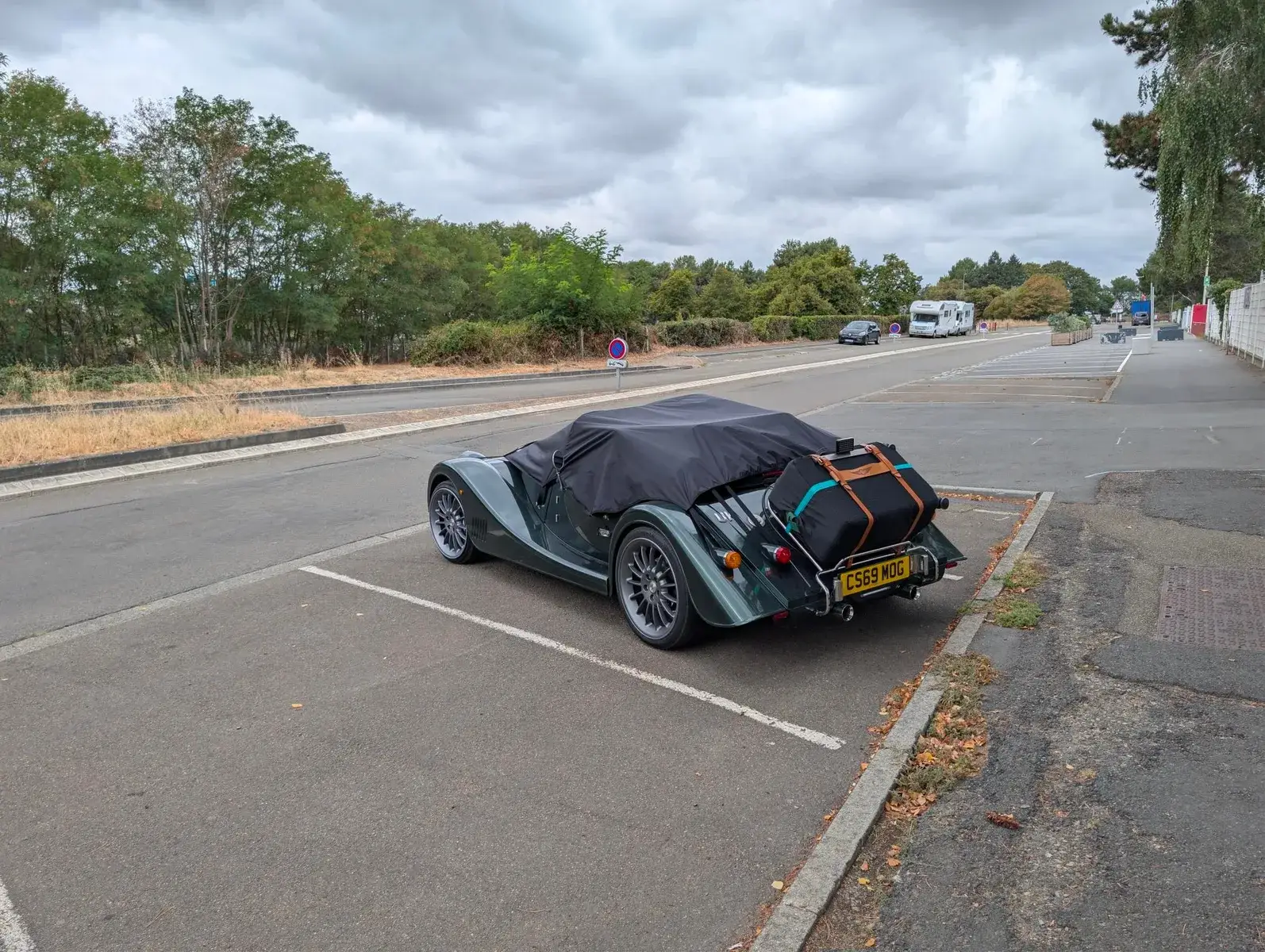 A vintage open-top sports car beside a race circuit
