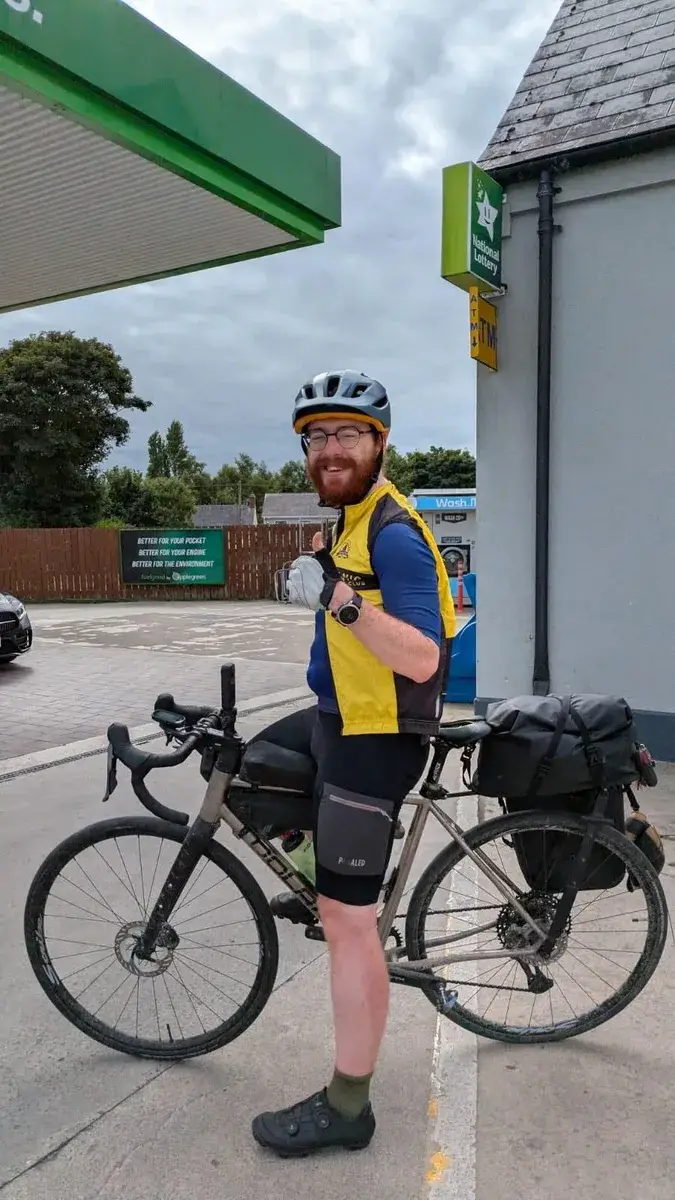 Neil smiling beside his loaded touring bicycle at the journey's end
