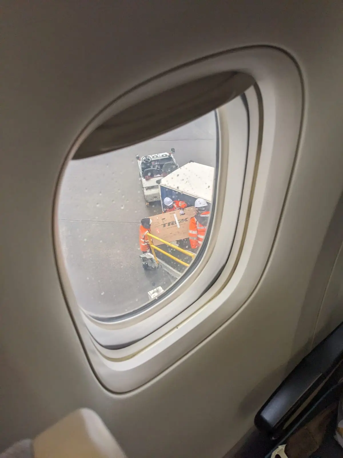 A bike box sitting on an airport tarmac beside luggage trolleys, seen from an aircraft window