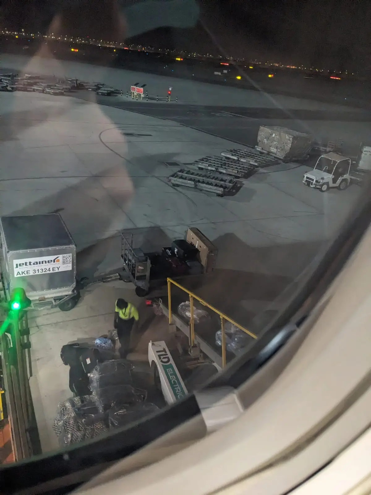 A bike box and luggage cart on an airport tarmac, seen through an aircraft window with staff nearby