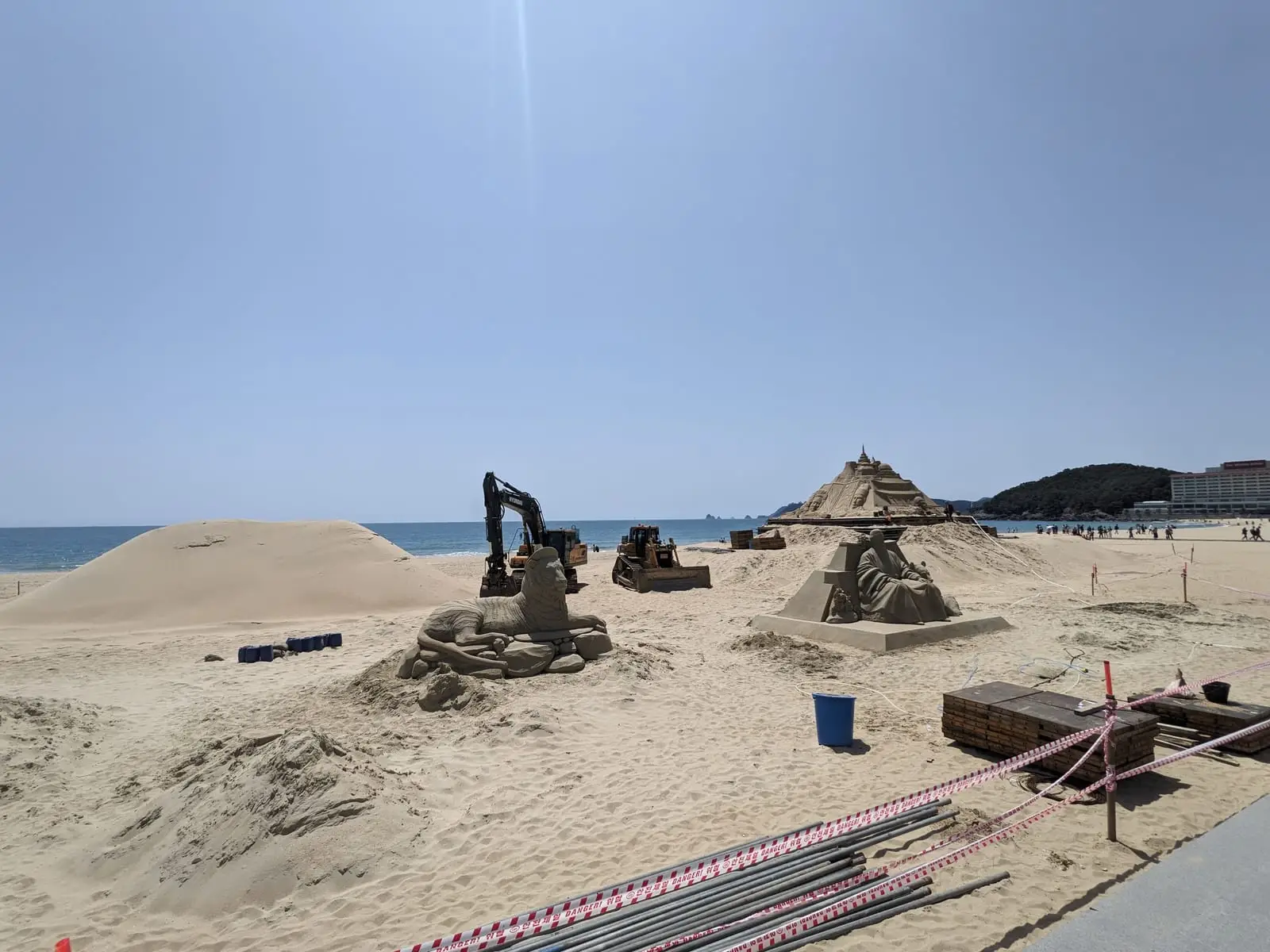 A sandy beach with elaborate sand sculptures, including one resembling a digger, under a shelter