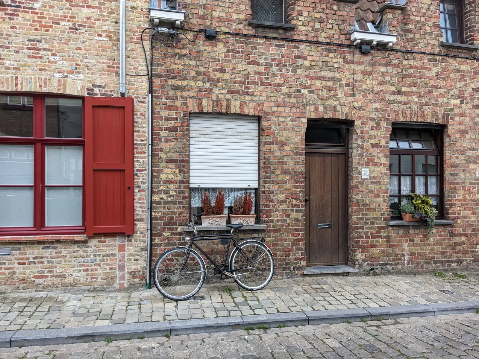 A bicycle leaning against a brick house with red shutters on a cobbled street in Bruges