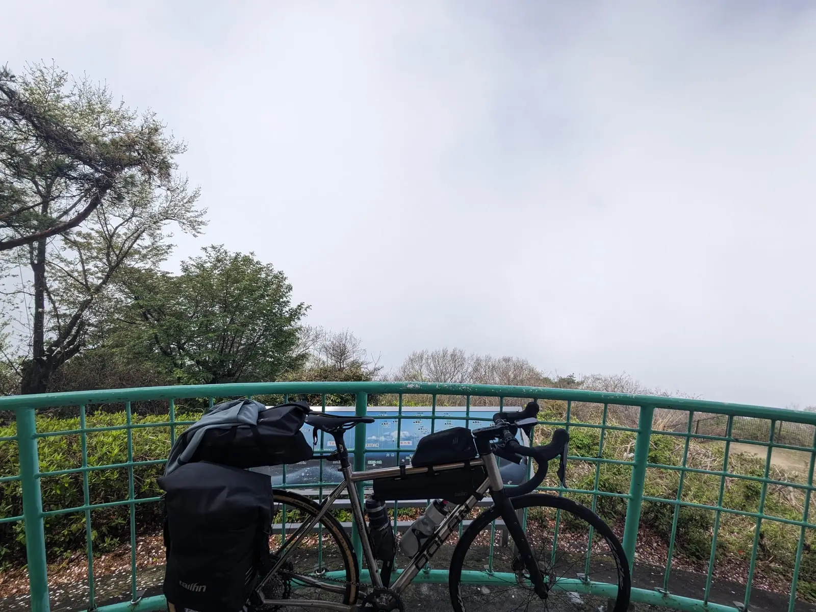 A loaded bike leaning against a railing above a valley shrouded in thick fog