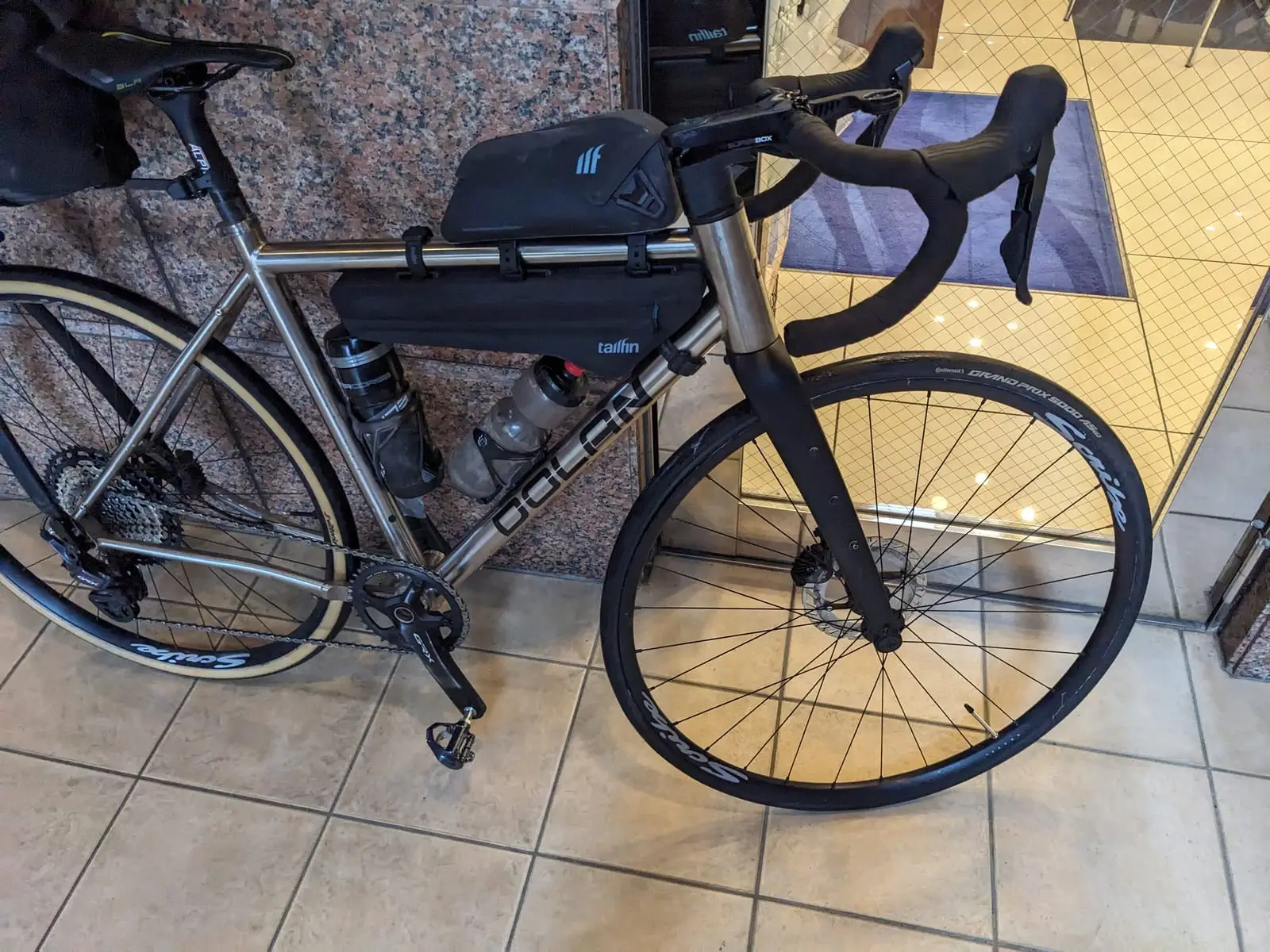 The loaded touring bike leaning against a wall indoors after fitting the replacement tyre