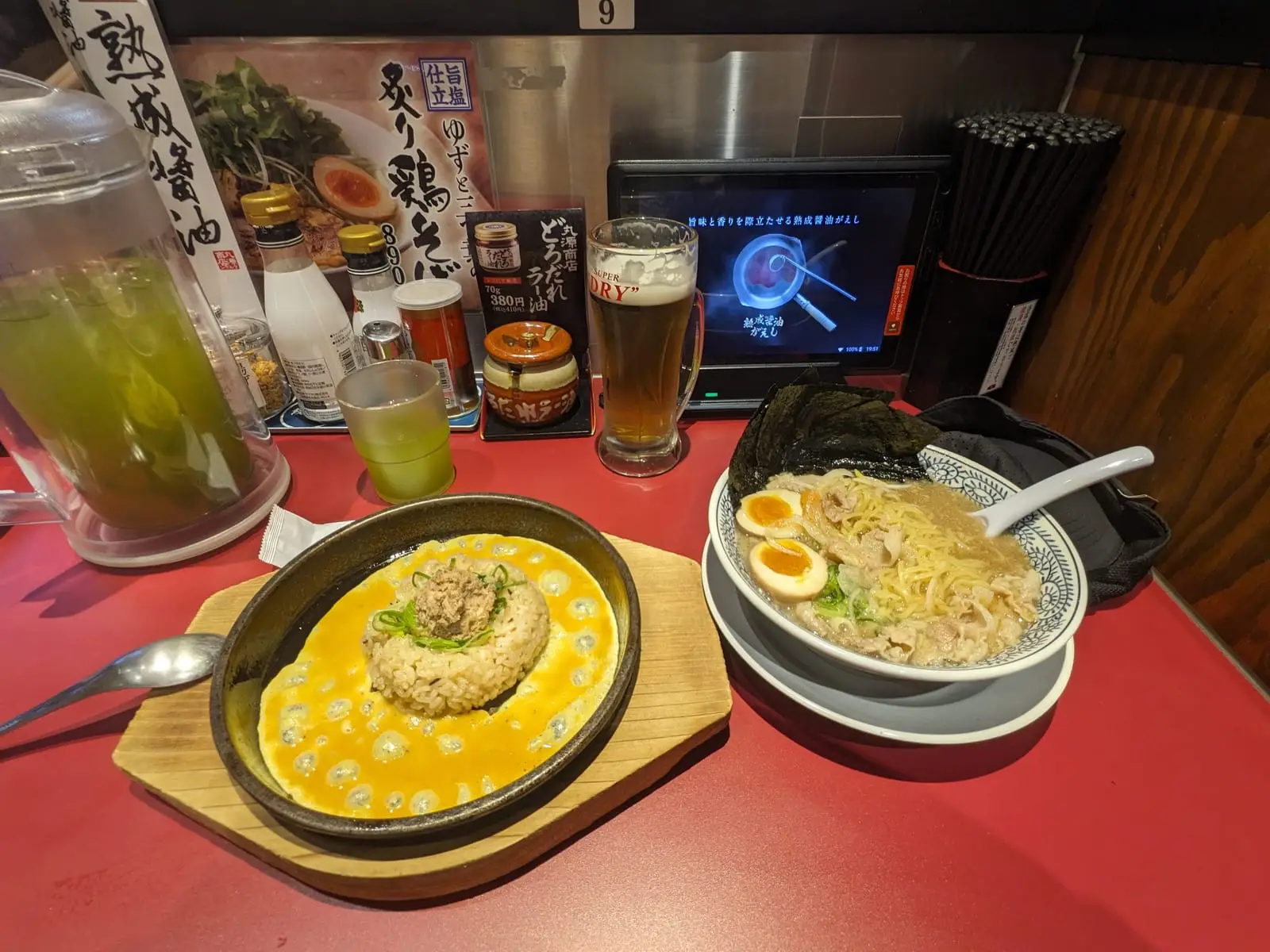 A bowl of ramen with a fried egg, served alongside a small rice dish and drinks on a restaurant table