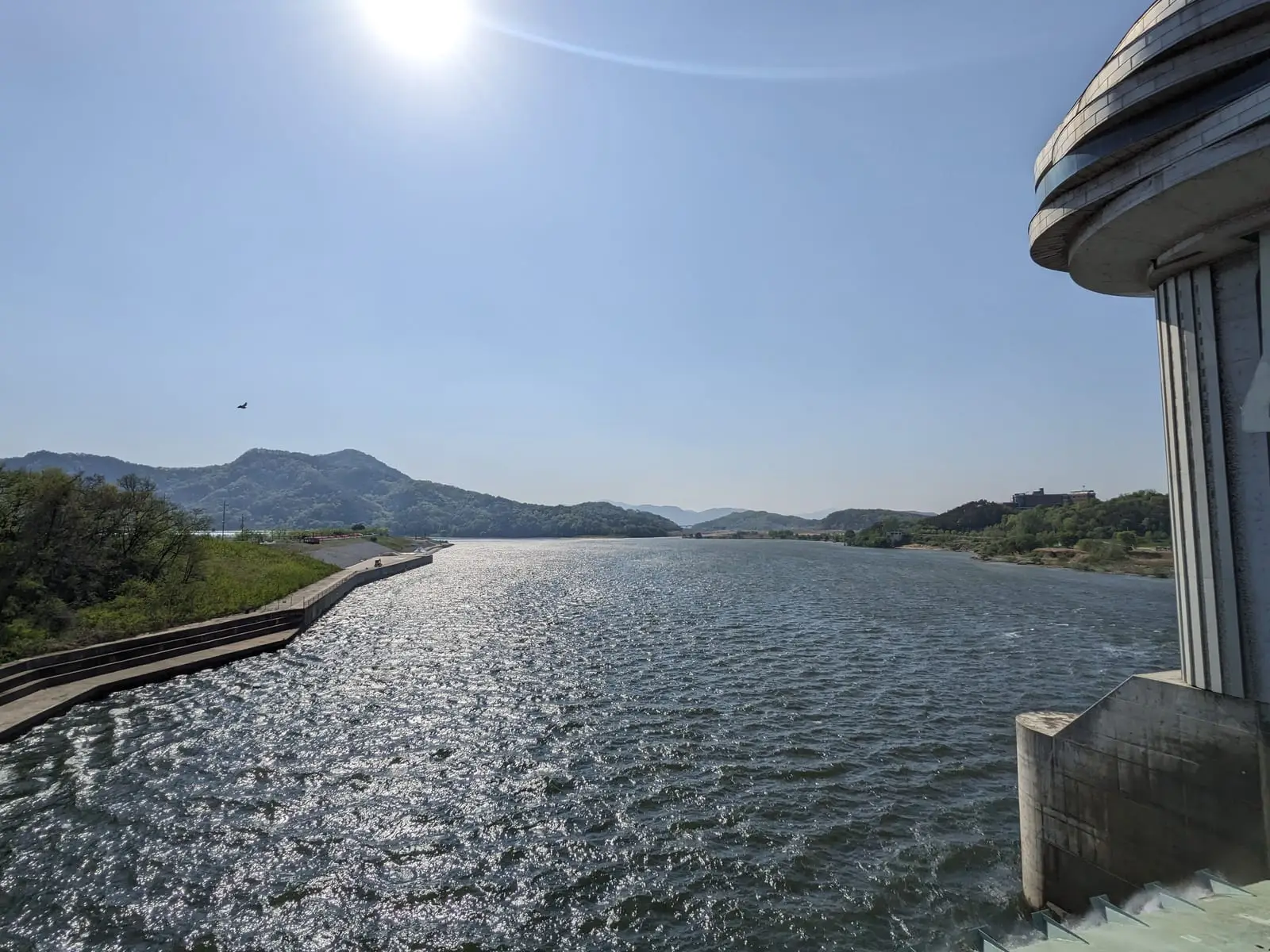 A view along a bridge railing over a wide river with hills in the distance