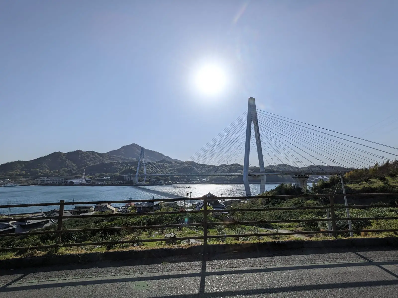 A cable-stayed bridge over glittering water, seen with the sun low over the sea