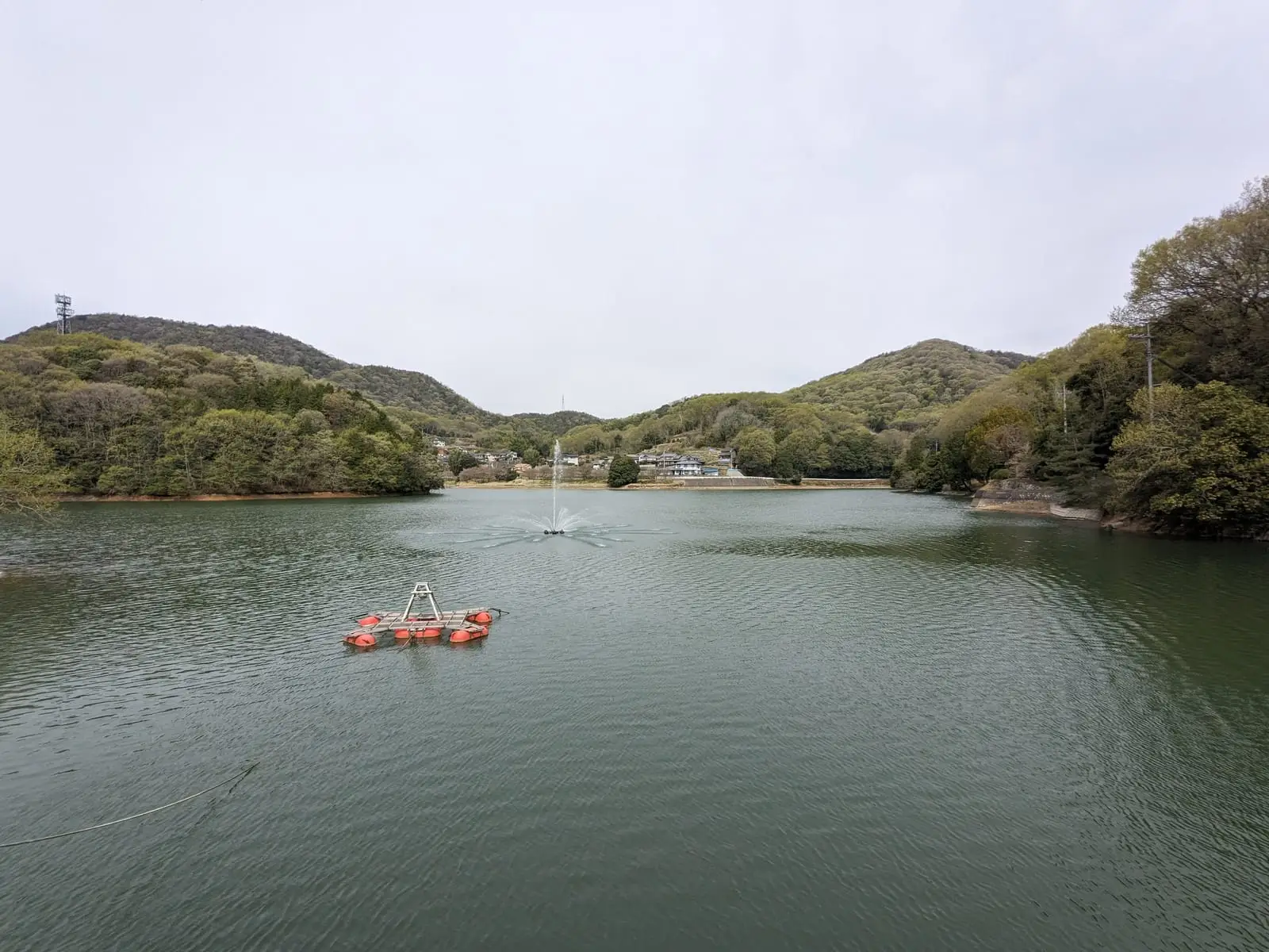 A calm reservoir surrounded by green hills, with a small red marker buoy floating on the water