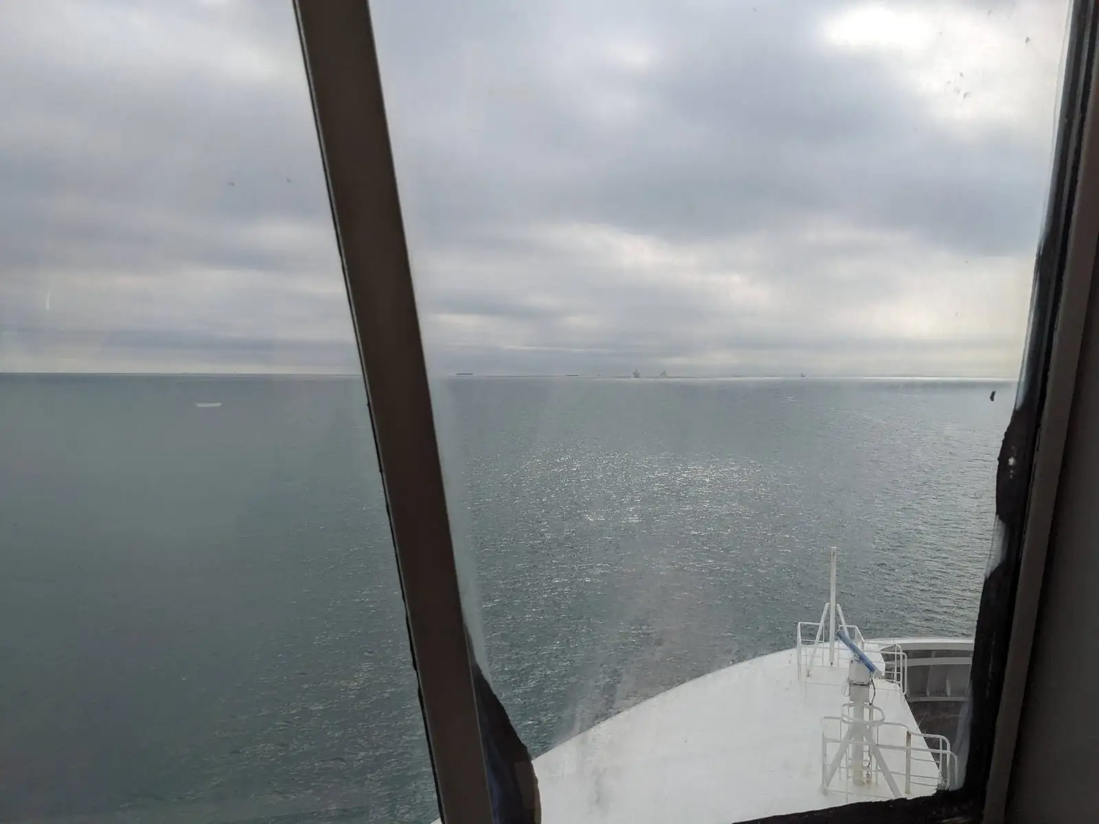 A flat grey sea and the ferry’s white bow, seen through a salt-streaked window