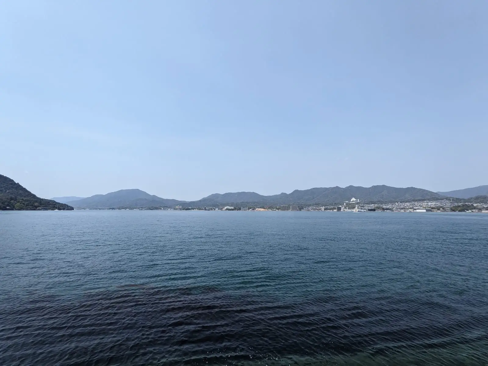 A calm sea view with a hazy coastline and small islands on the horizon