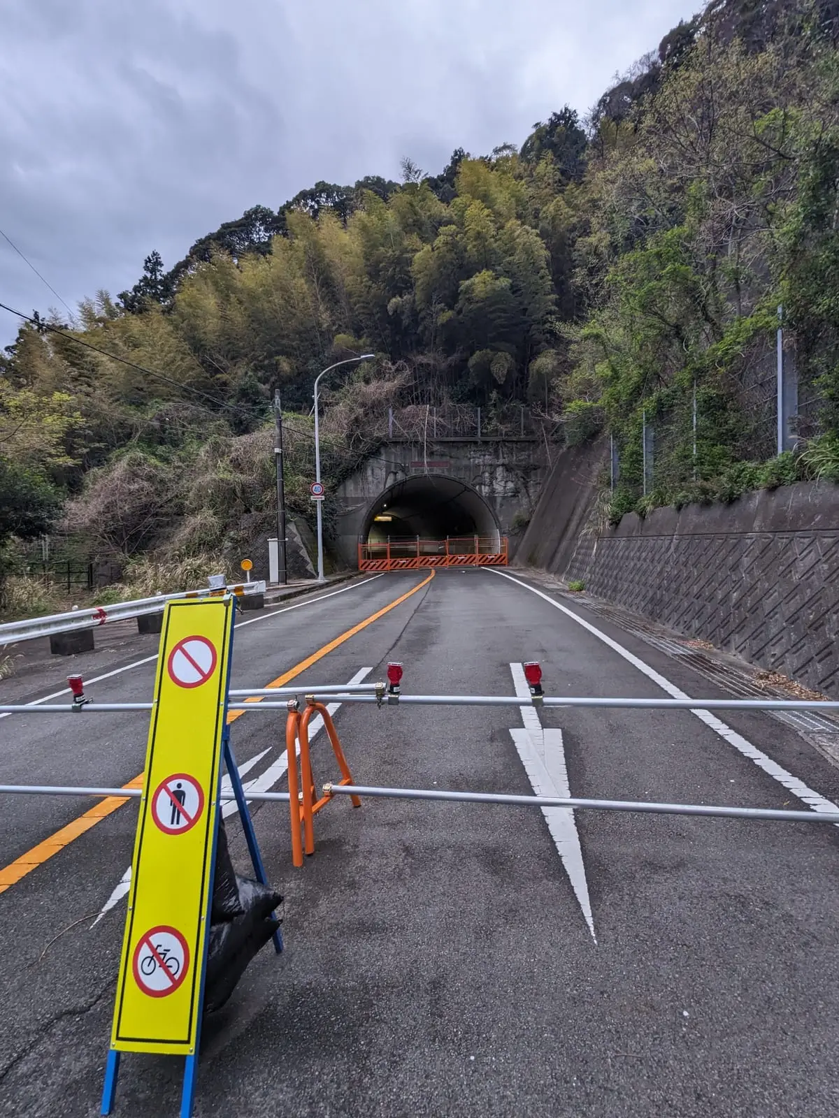 A closed tunnel entrance blocked by barriers and warning signs on an empty road