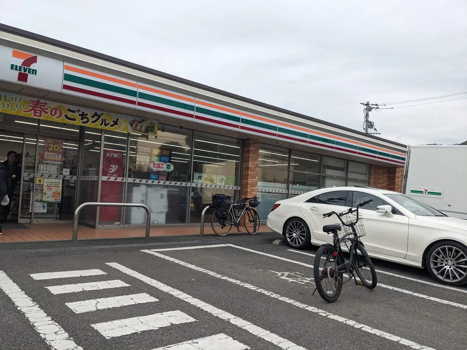 A Japanese convenience store storefront with a car and a bicycle parked outside