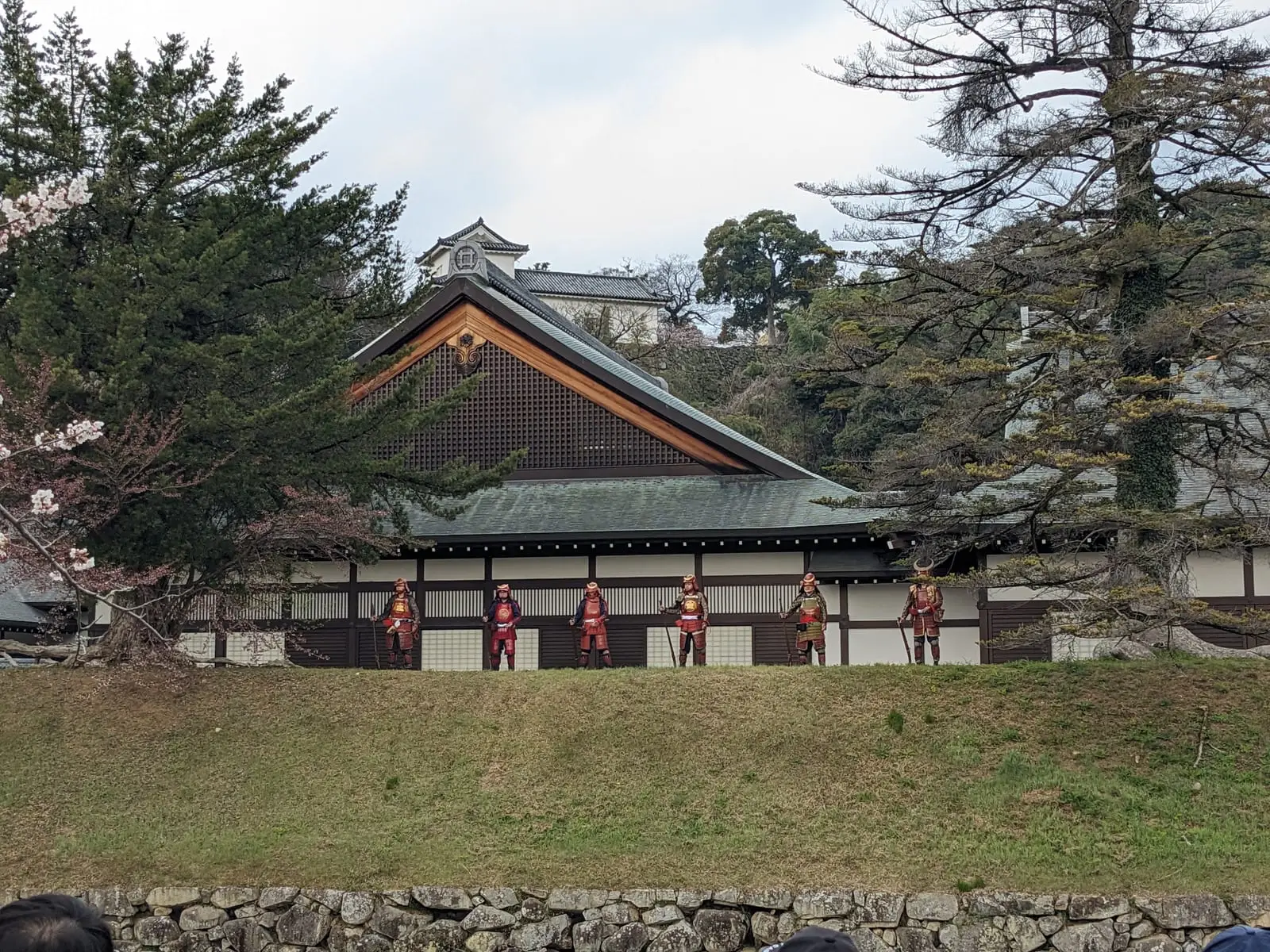 A row of performers in red-and-white samurai-style costume standing on the grass in front of a traditional building