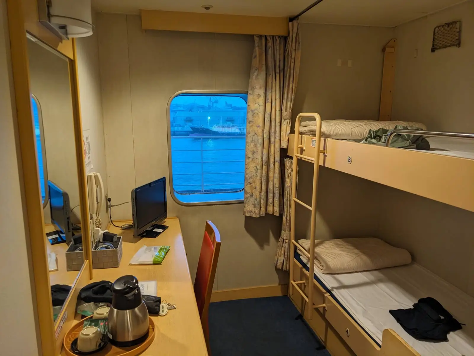 A small ferry cabin interior with bunk beds, a wall-mounted television, and a desk