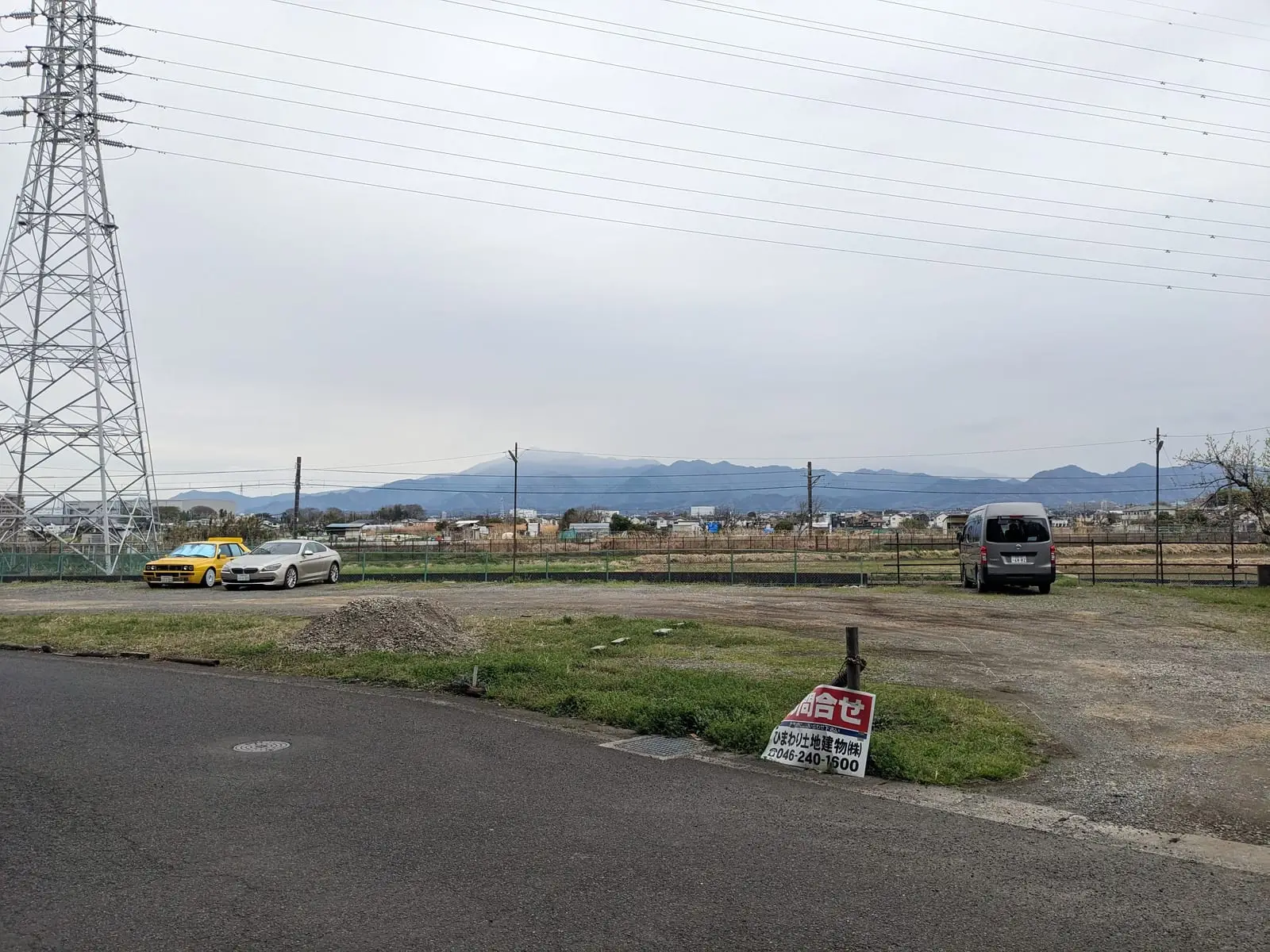A rural road with power lines leading toward low hills on the horizon