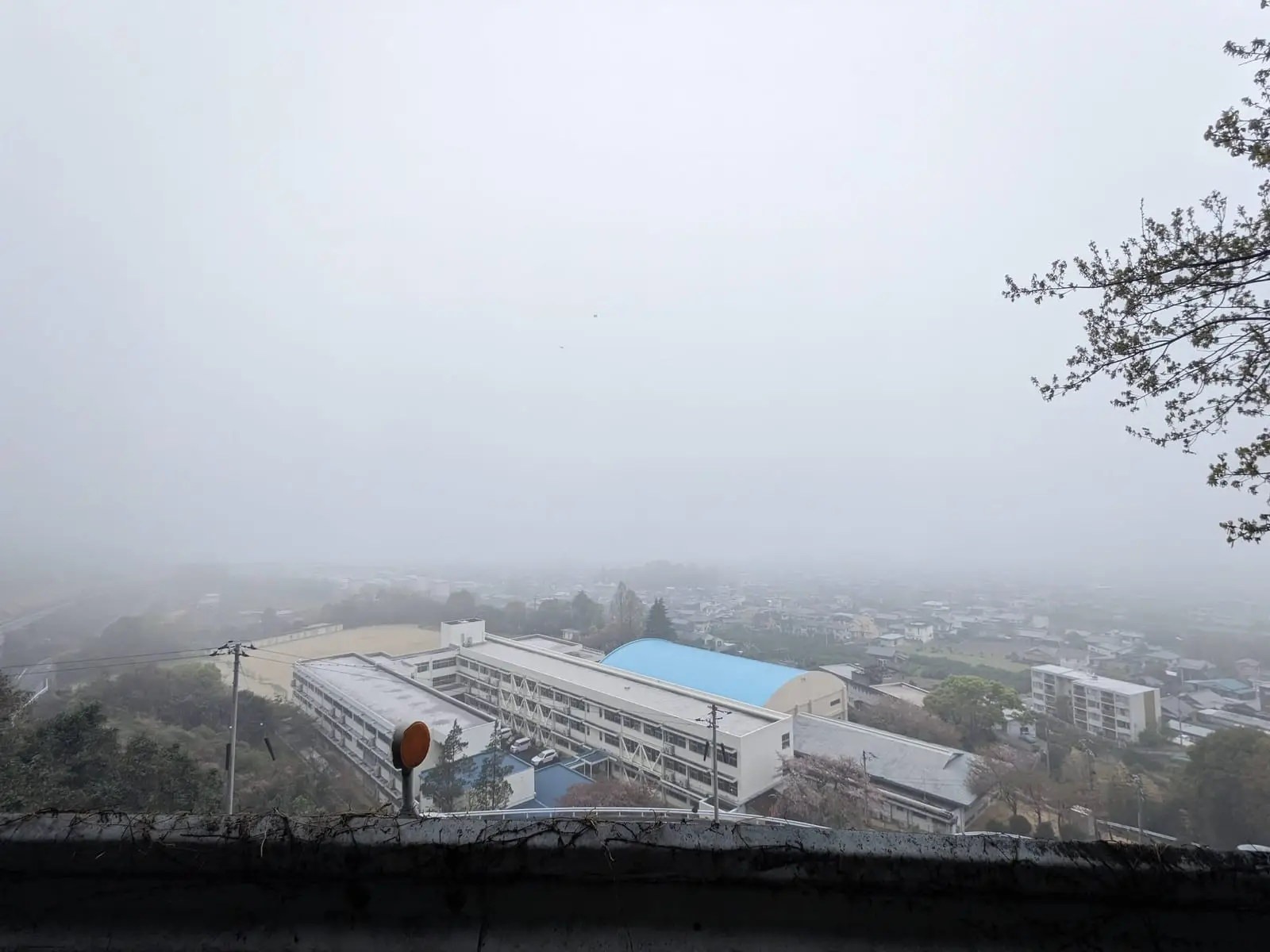 A hillside town shrouded in fog, seen from a high vantage point with a large building below