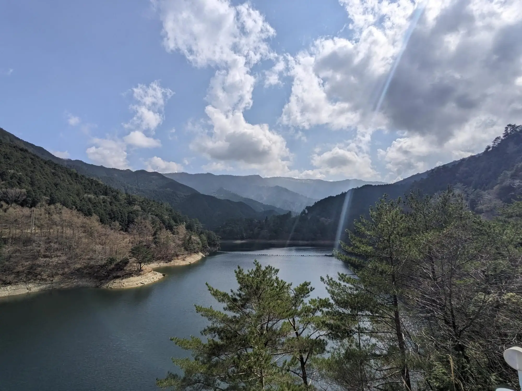 A forested mountain valley with a reservoir under a partly cloudy sky
