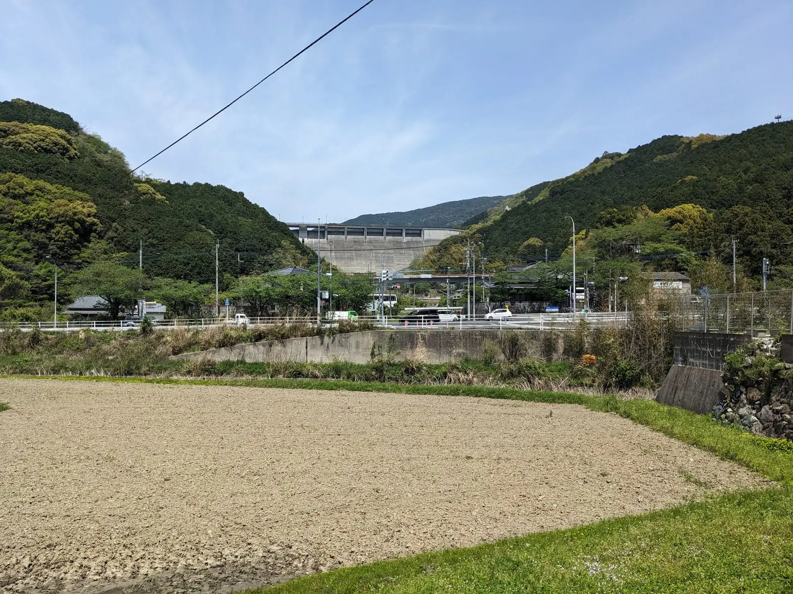 Green terraced fields with a large dam structure and hills in the distance