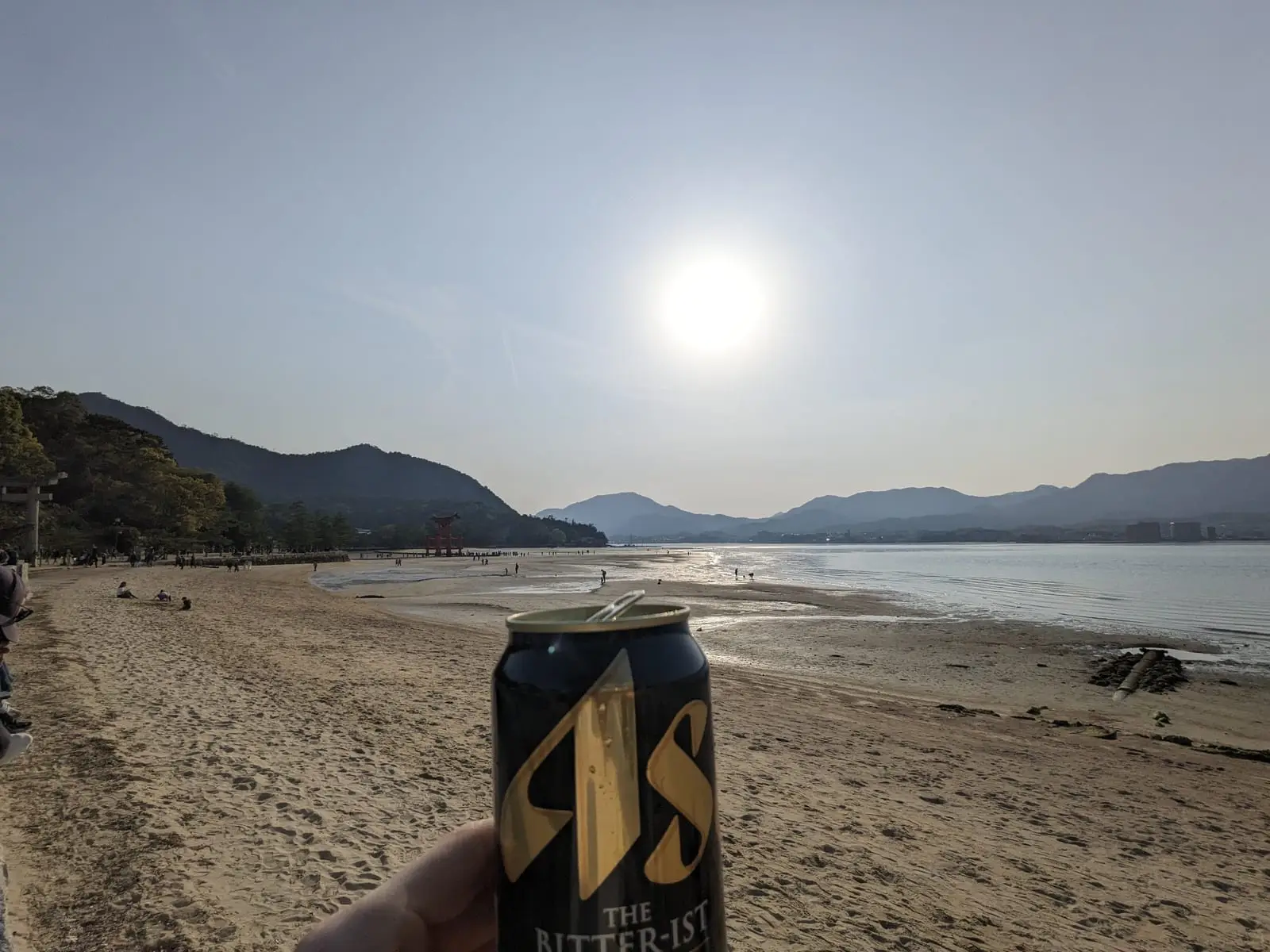 A hand holding a drink can in silhouette against the sun setting over the bay