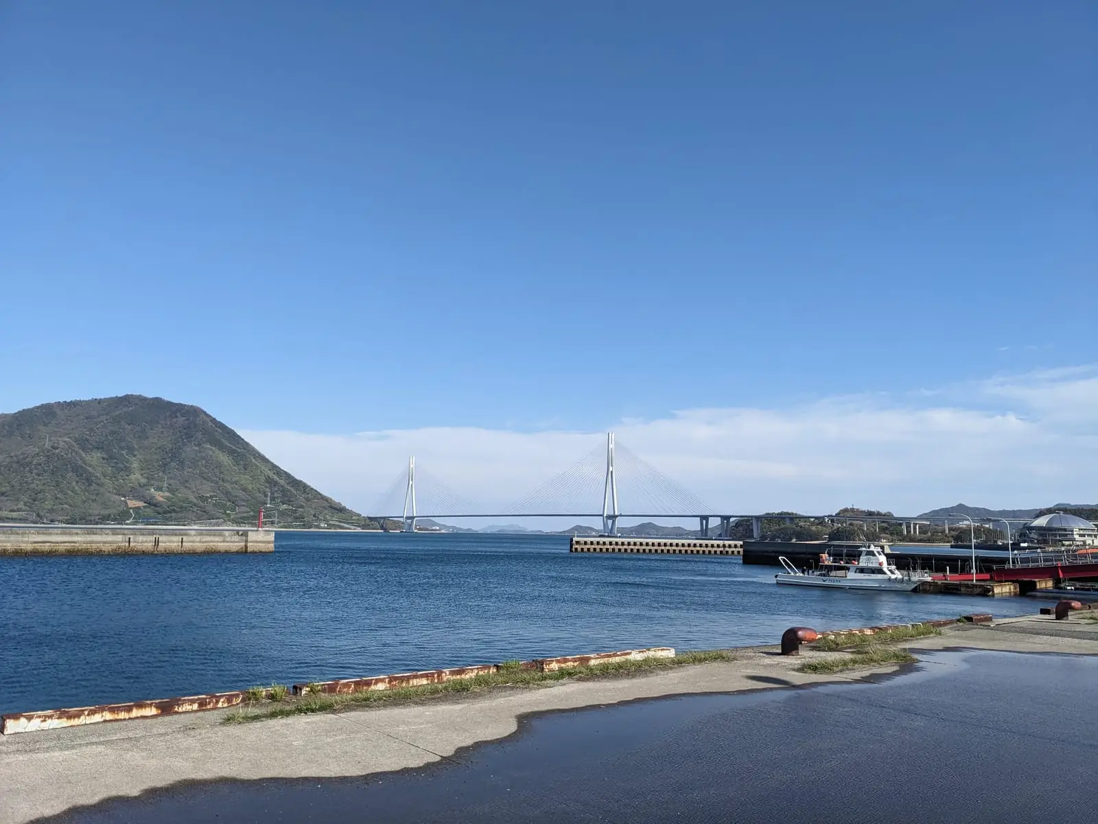 A small harbour with moored boats beneath a conical island hill on the Shimanami Kaido route