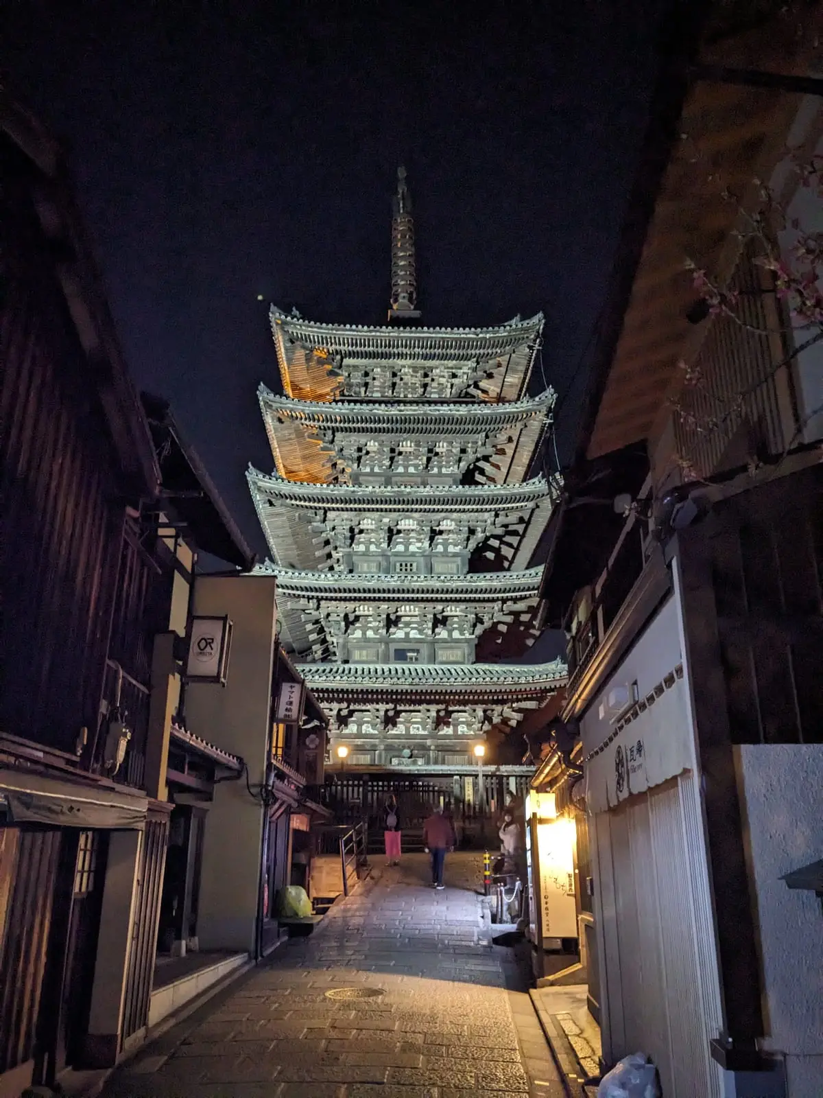 A traditional five-storey pagoda illuminated at night among Kyoto’s older buildings