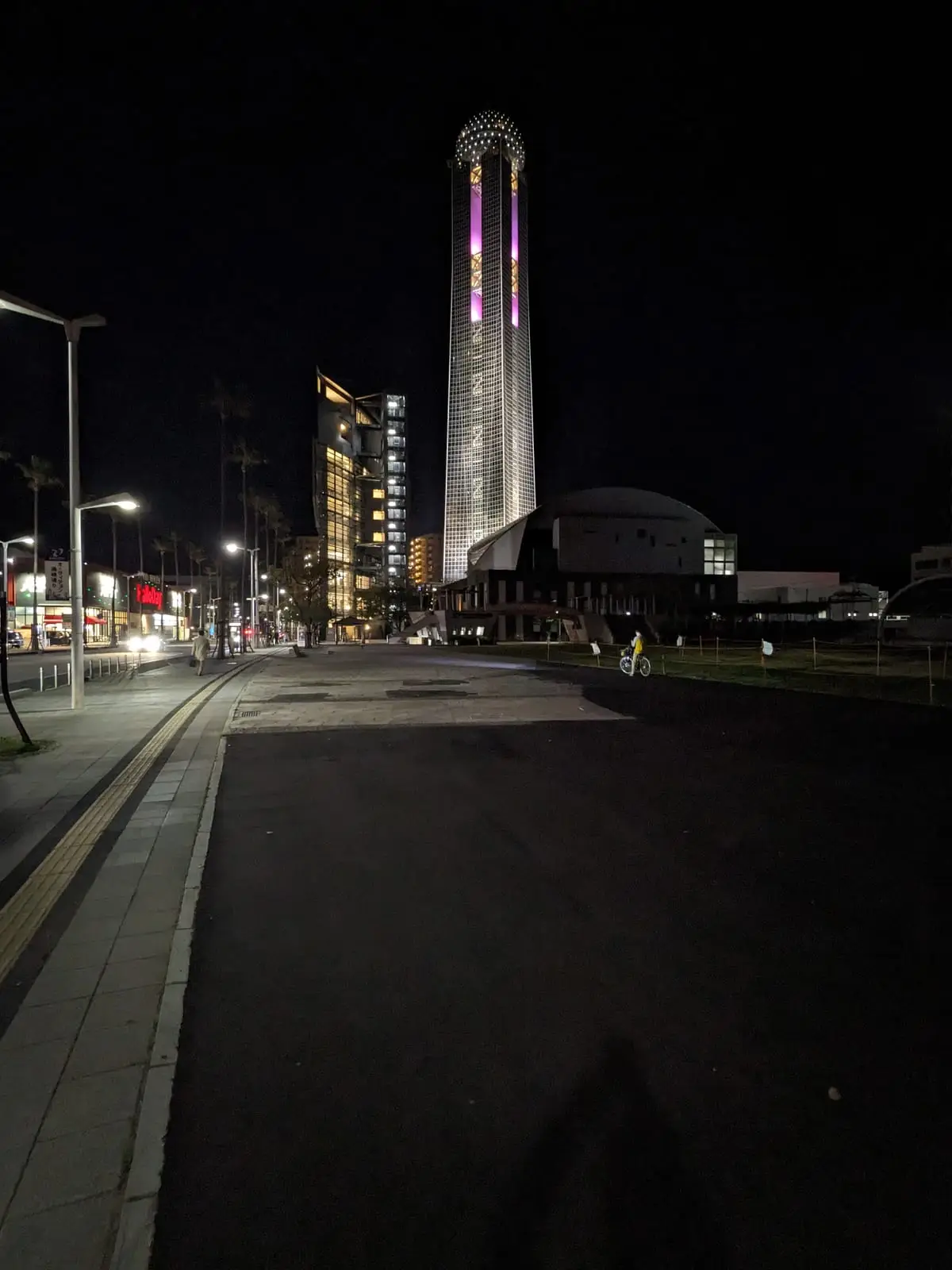 An illuminated tower building glowing orb-like at night above an empty street