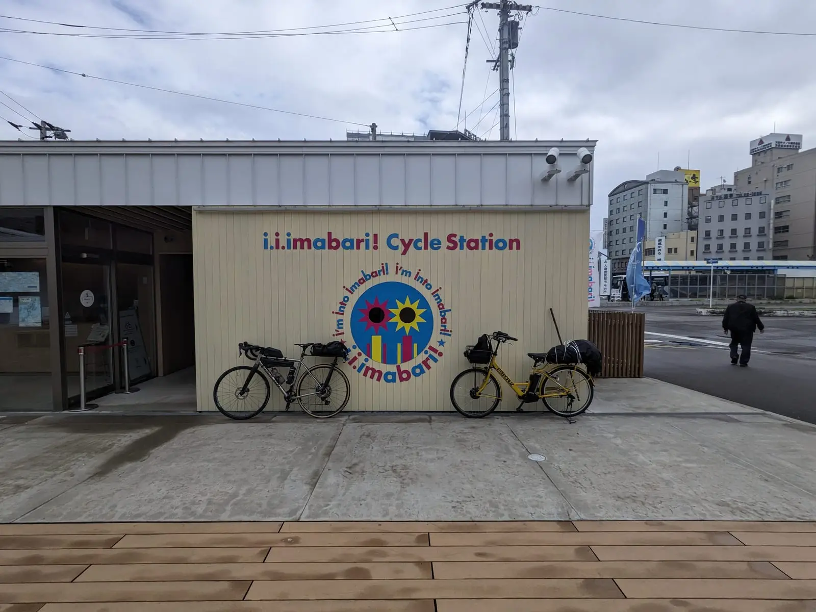 The Imabari Cycle Station building with loaded touring bikes parked outside and a cyclist walking past