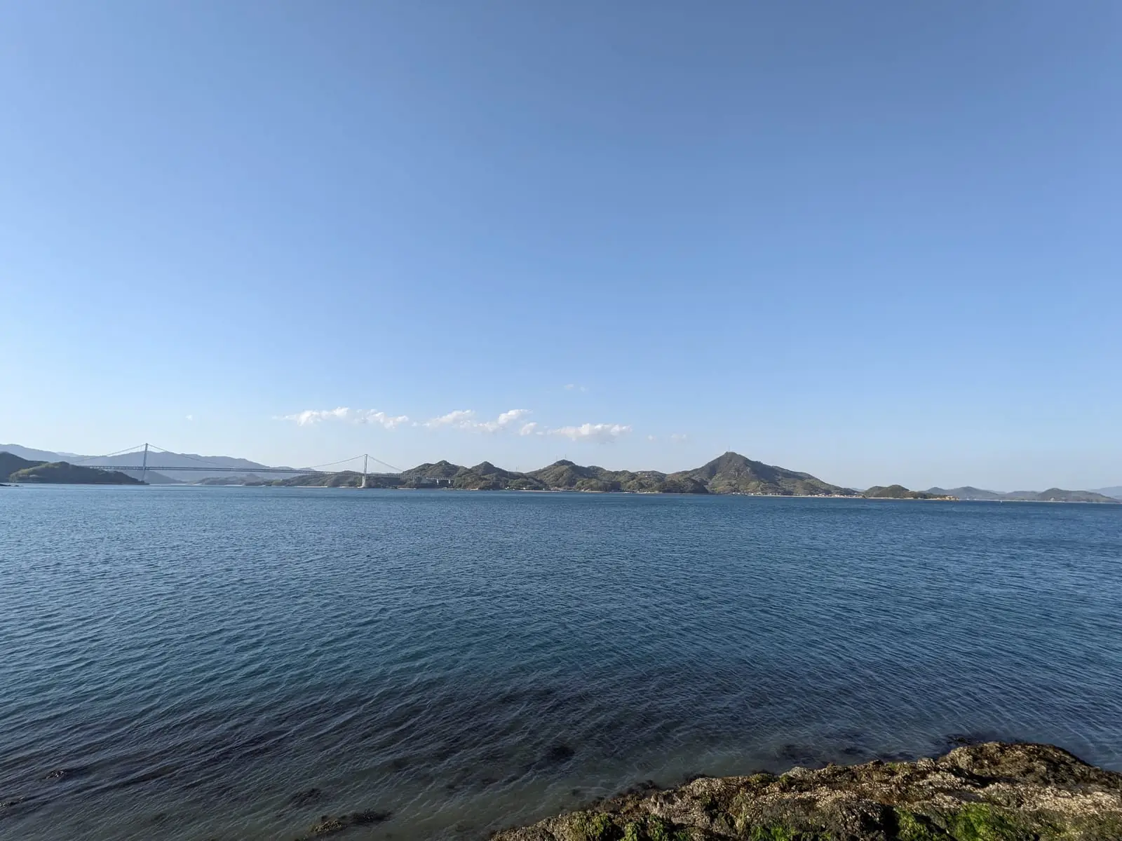 Small green islands scattered across calm blue water, seen from a Shimanami Kaido bridge.
