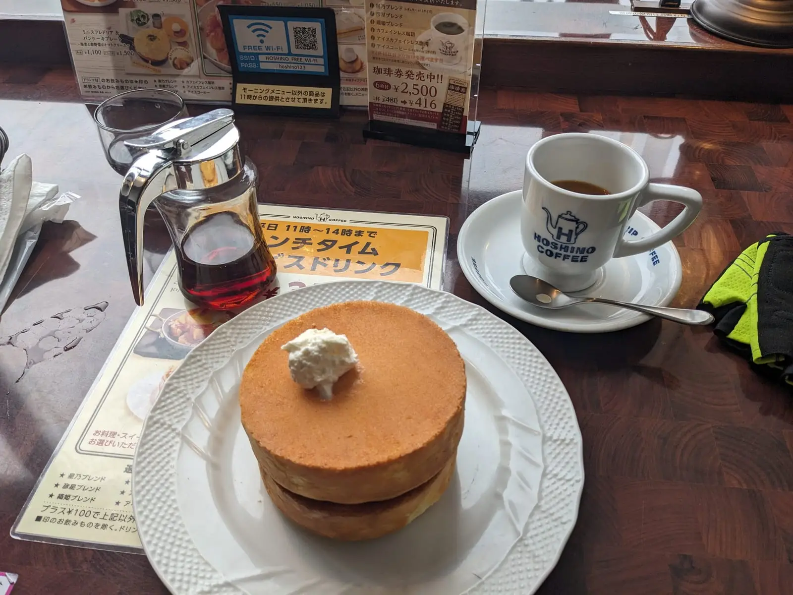 A stack of fluffy Japanese-style pancakes with syrup, served alongside a coffee on a café table
