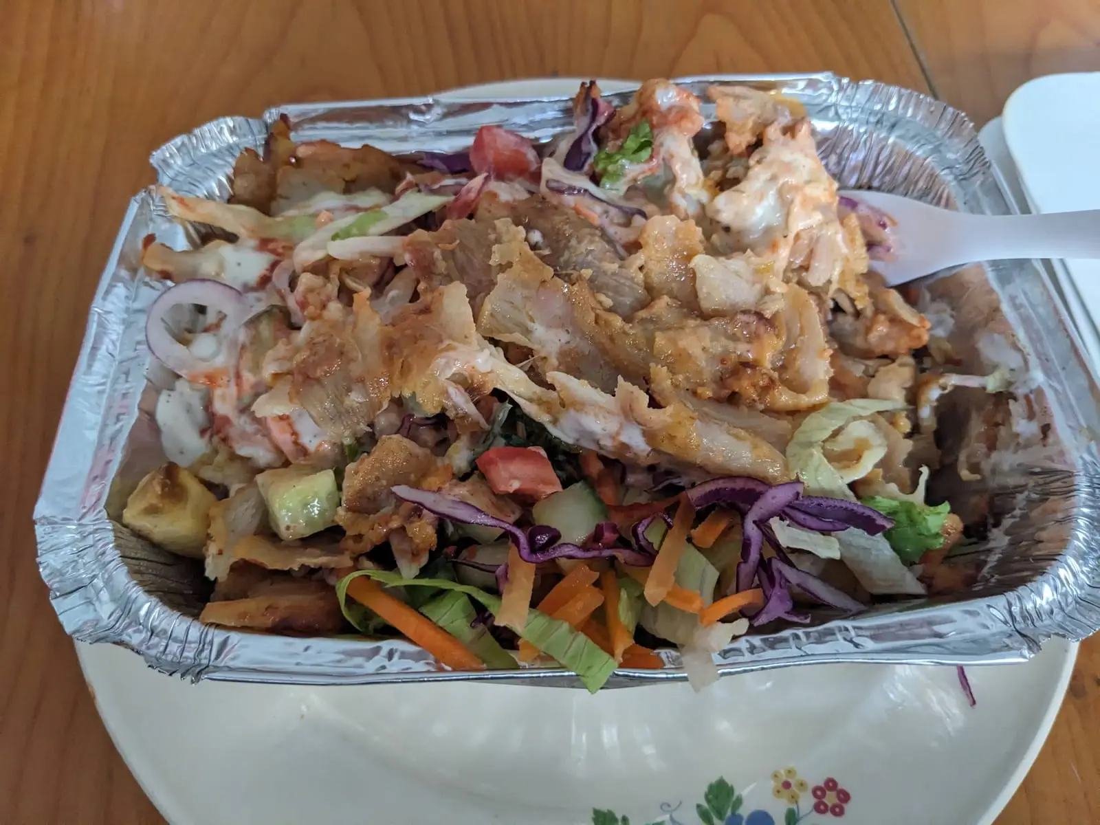 A tray of kapsalon topped with meat, salad, and sauce