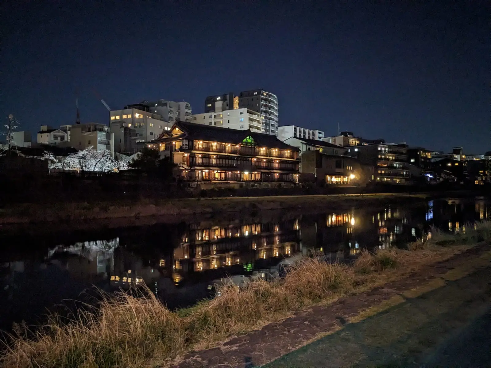 A traditional building lit up at night, reflected in a still canal in Kyoto