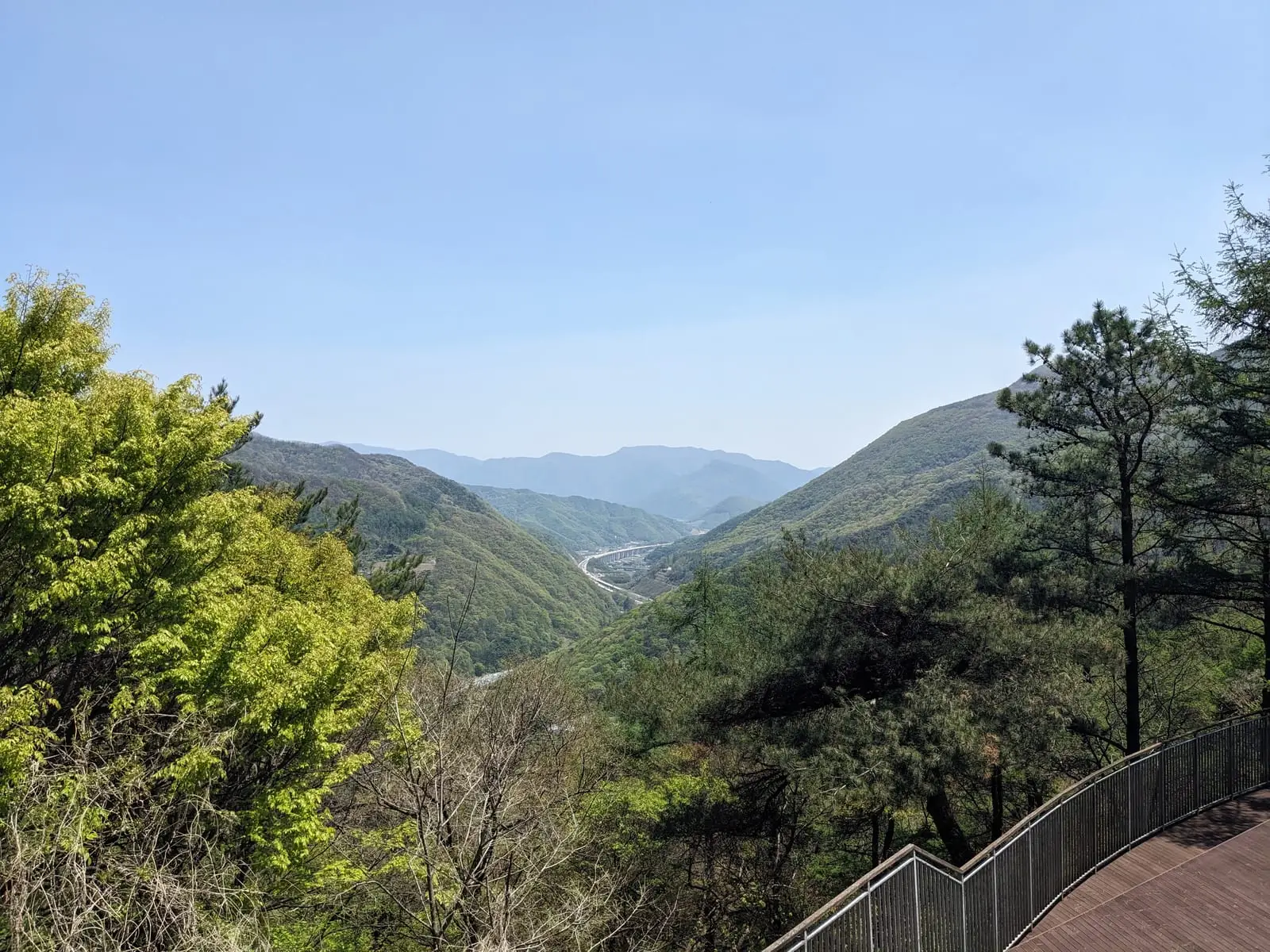 A layered green mountain valley seen from a viewpoint, with a road winding along the valley floor below