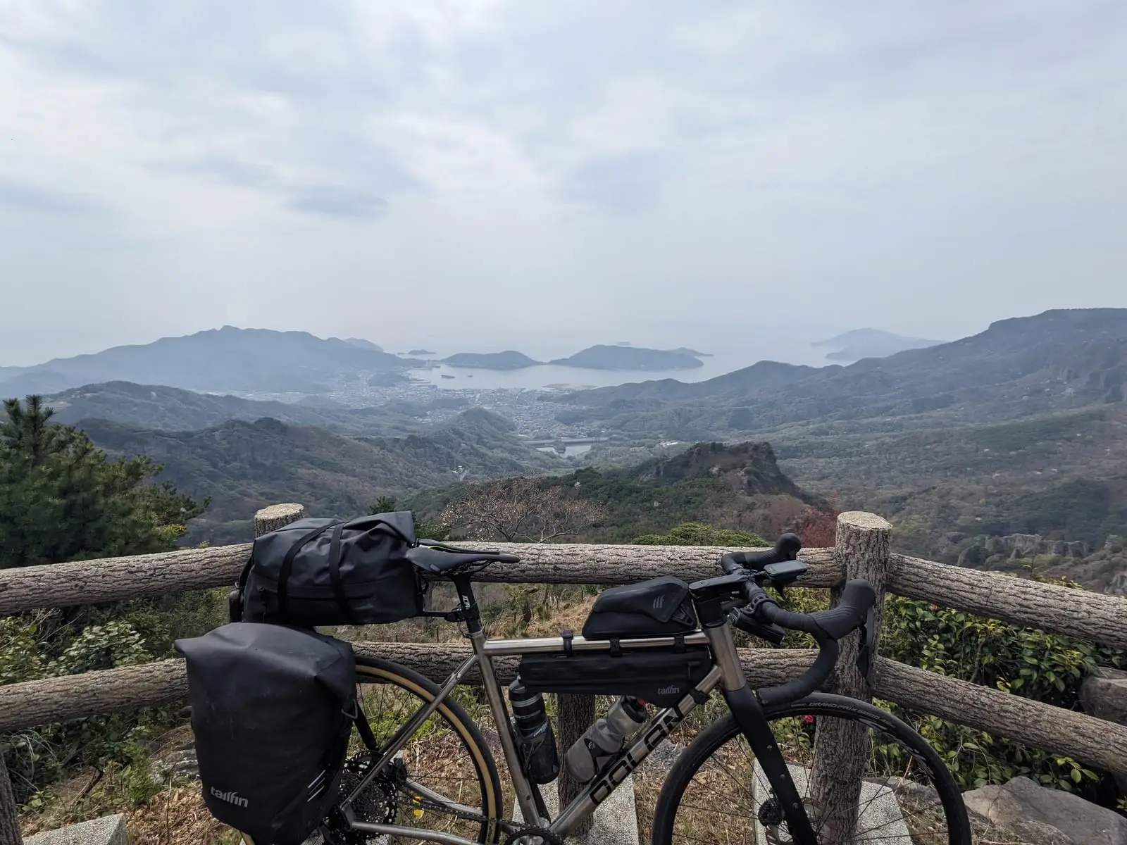 A loaded touring bike leaning against a wooden fence, overlooking misty layered hills