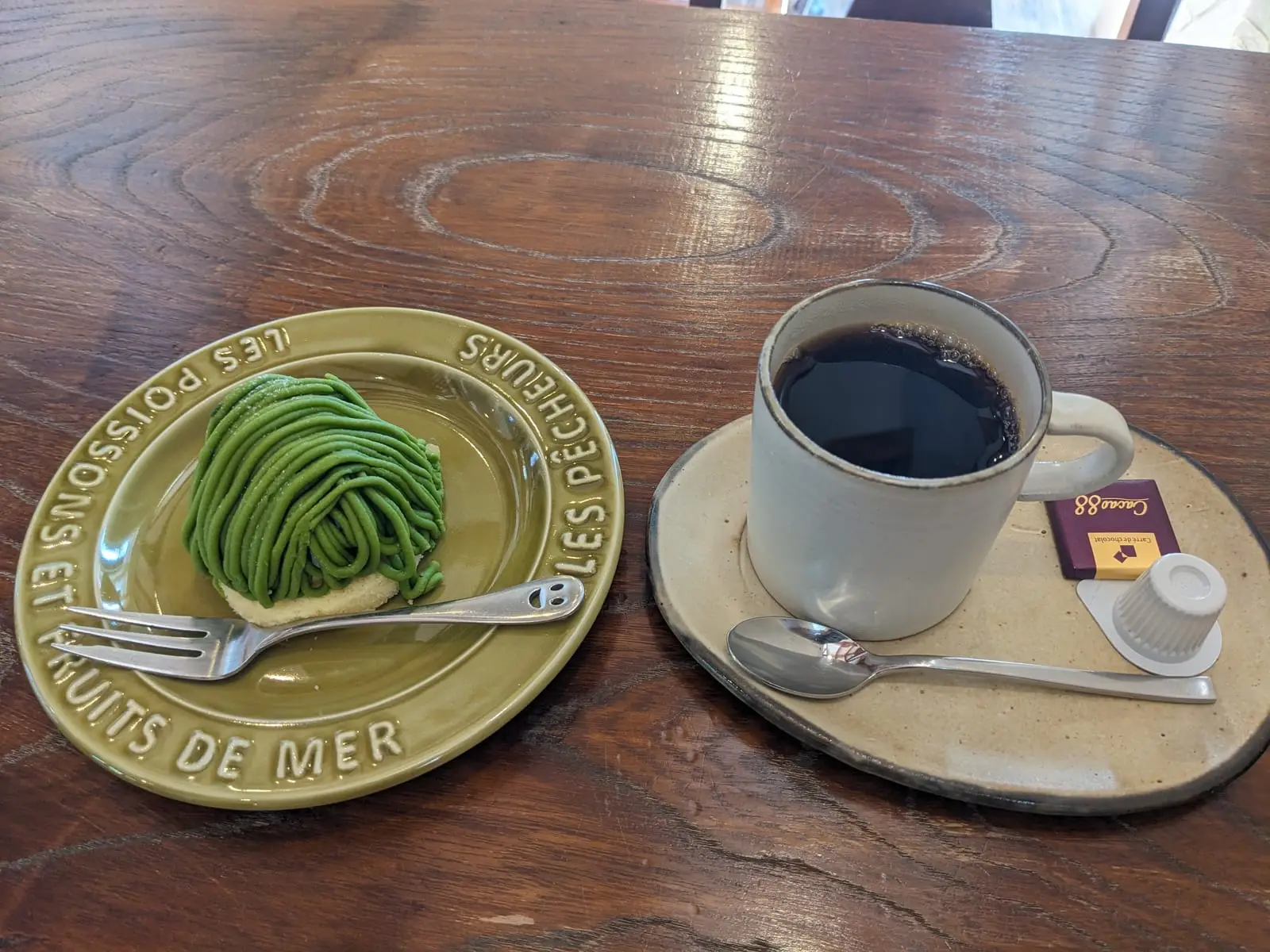 A green matcha cream roll dessert on a small plate with a fork, served on a café table