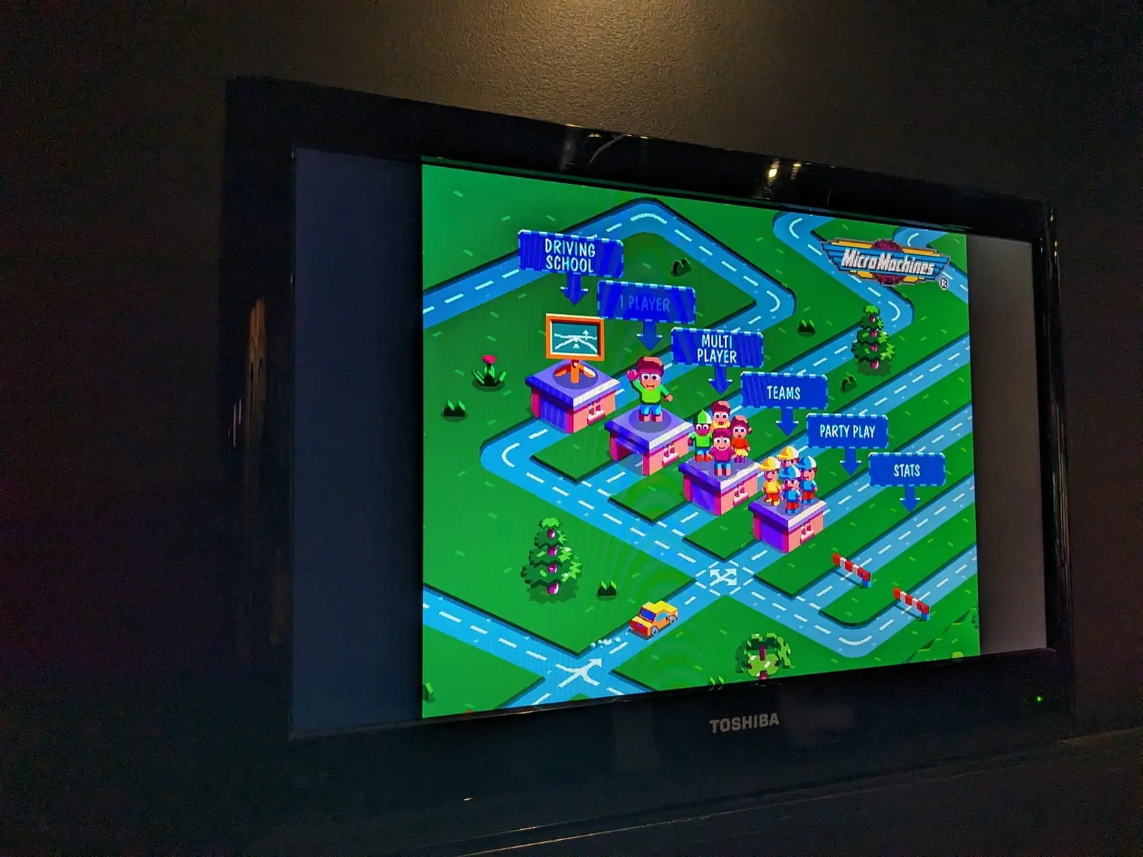 A television in a dark bar showing the Micro Machines menu