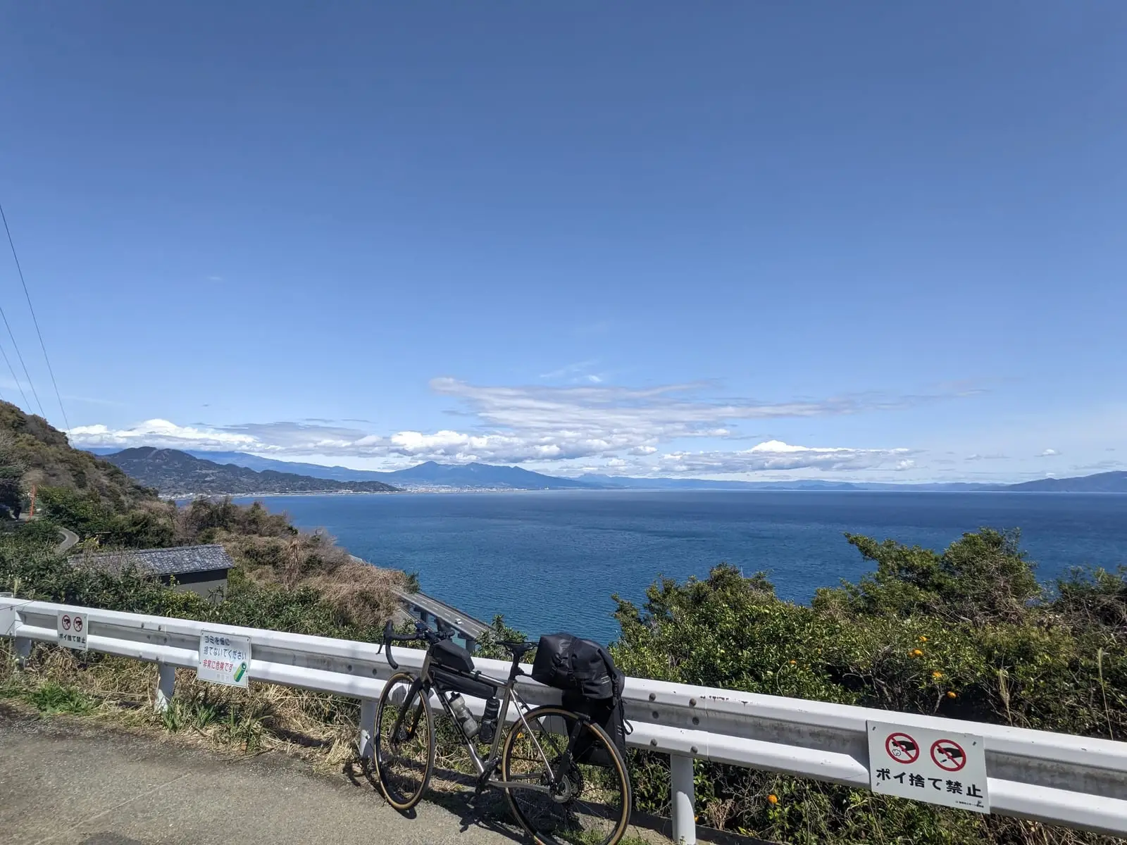 A loaded touring bike beside a guardrail, with Mount Fuji’s snow-capped peak just visible over distant hills