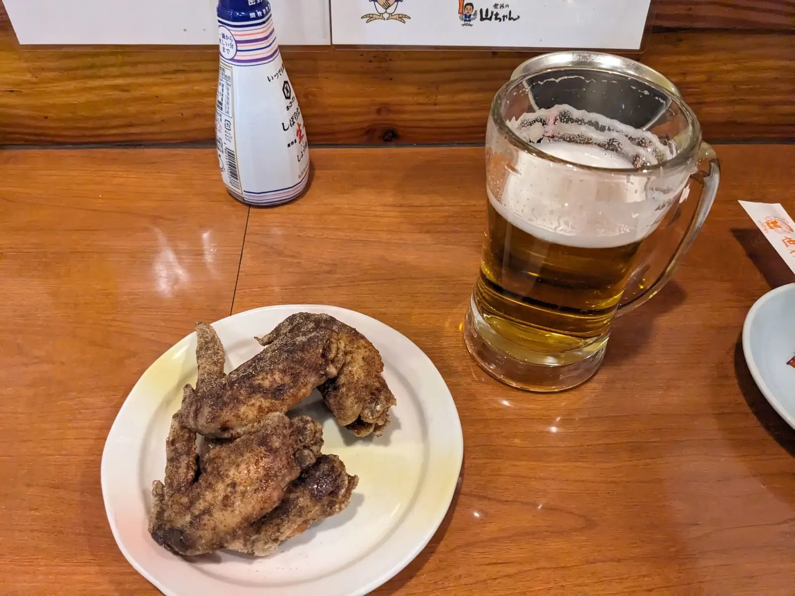 A plate of Nagoya-style fried chicken wings alongside a beer, a classic Nagoya dish