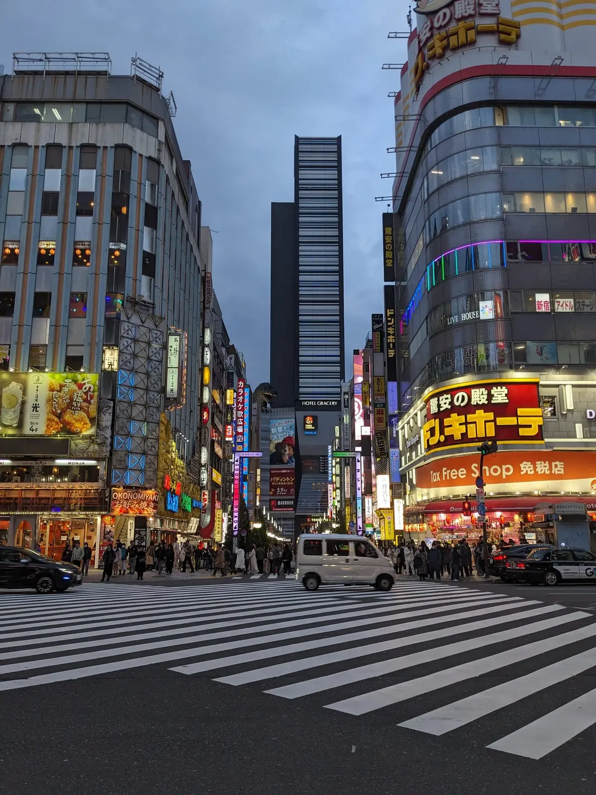 A neon-lit Tokyo street at night, crowded with pedestrians beneath illuminated shop signs