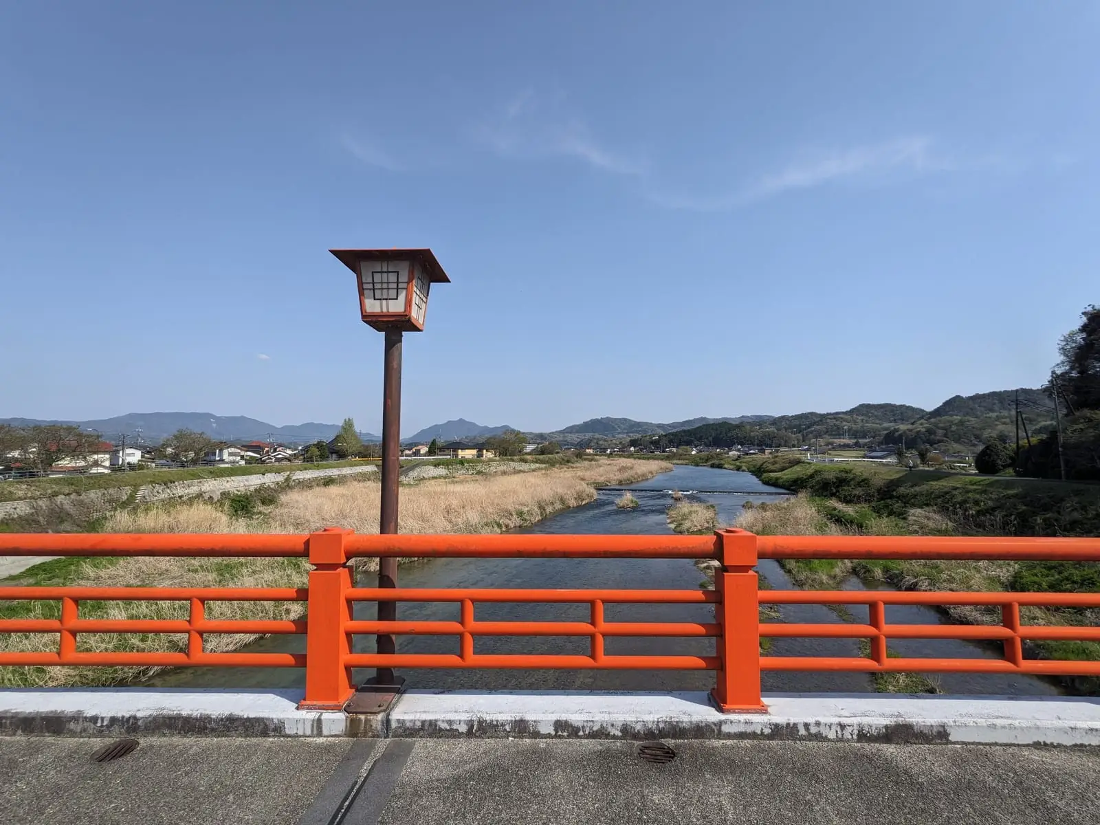 An ornate orange lamp post on a red bridge railing, overlooking a river and hills