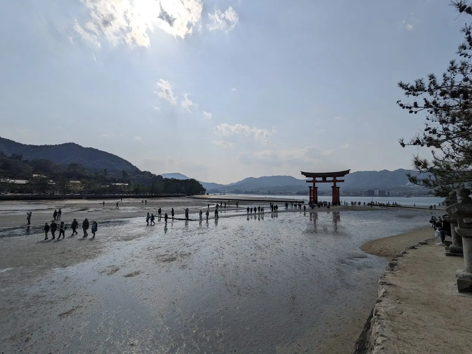 The Itsukushima floating torii gate seen across exposed mudflats at low tide, with people walking out to it