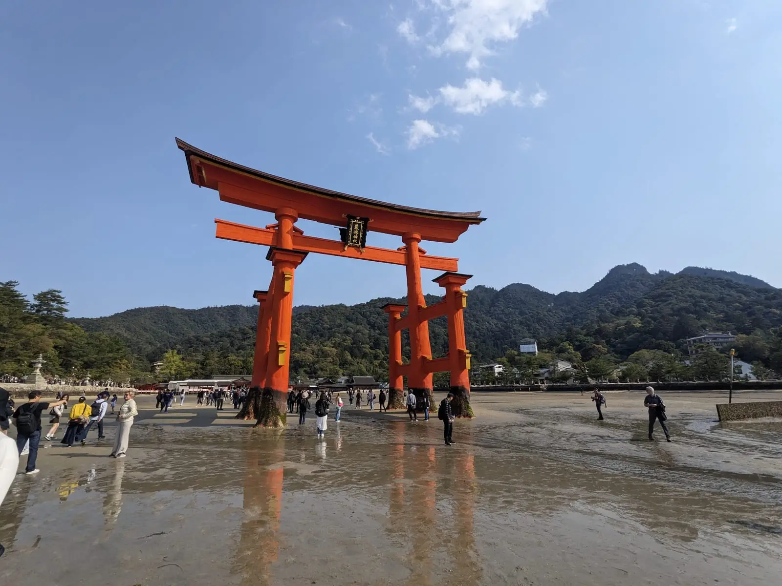 The large orange Otorii gate standing on the exposed mudflats, with visitors gathered at its base
