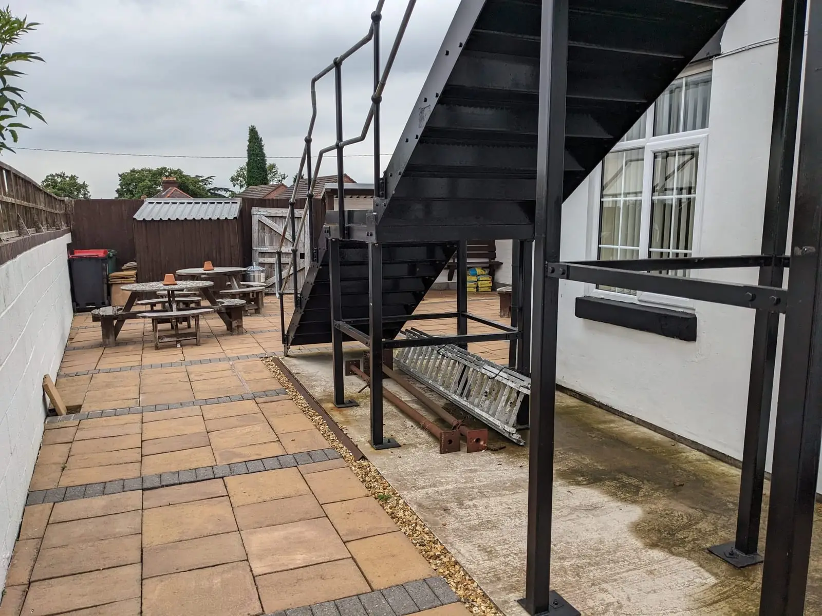 A black metal outdoor staircase beside a paved pub garden with picnic benches