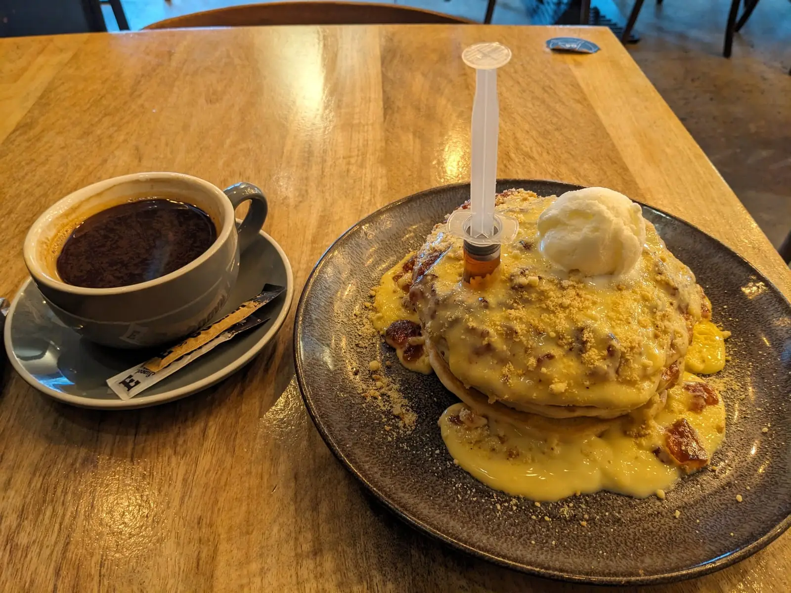 A stack of pancakes with sauce and ice cream beside a coffee