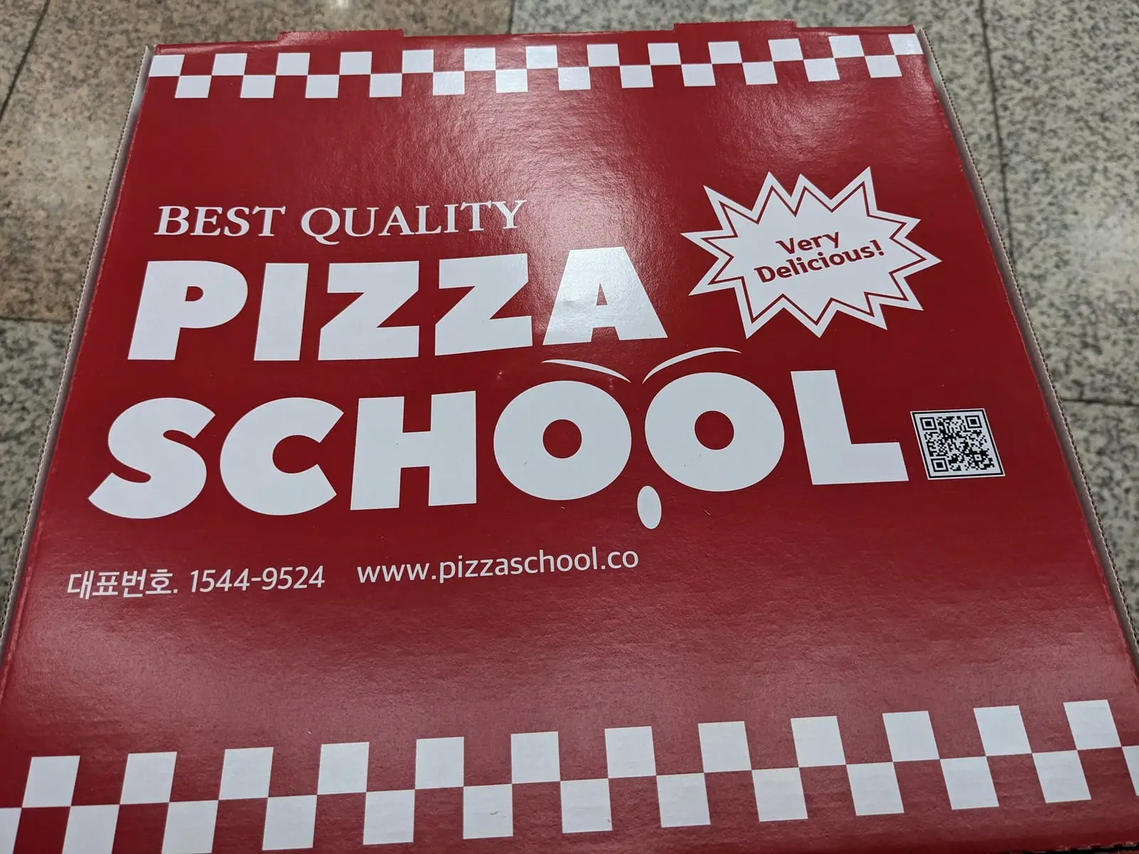 A red pizza box lid printed with the ‘Pizza School’ logo and a QR code