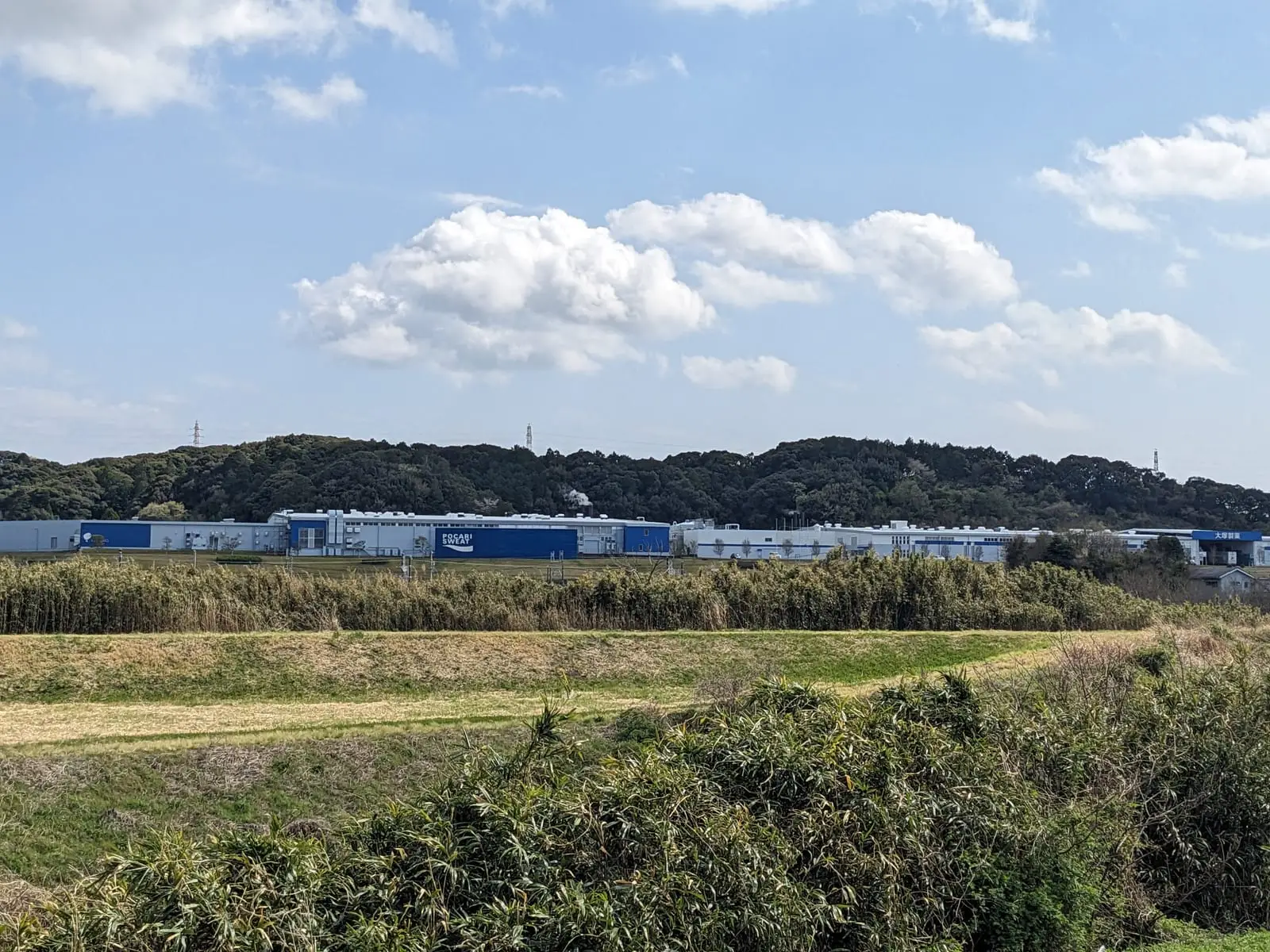 A large factory complex seen across open fields, identified in the ride notes as a Pocari Sweat drinks factory